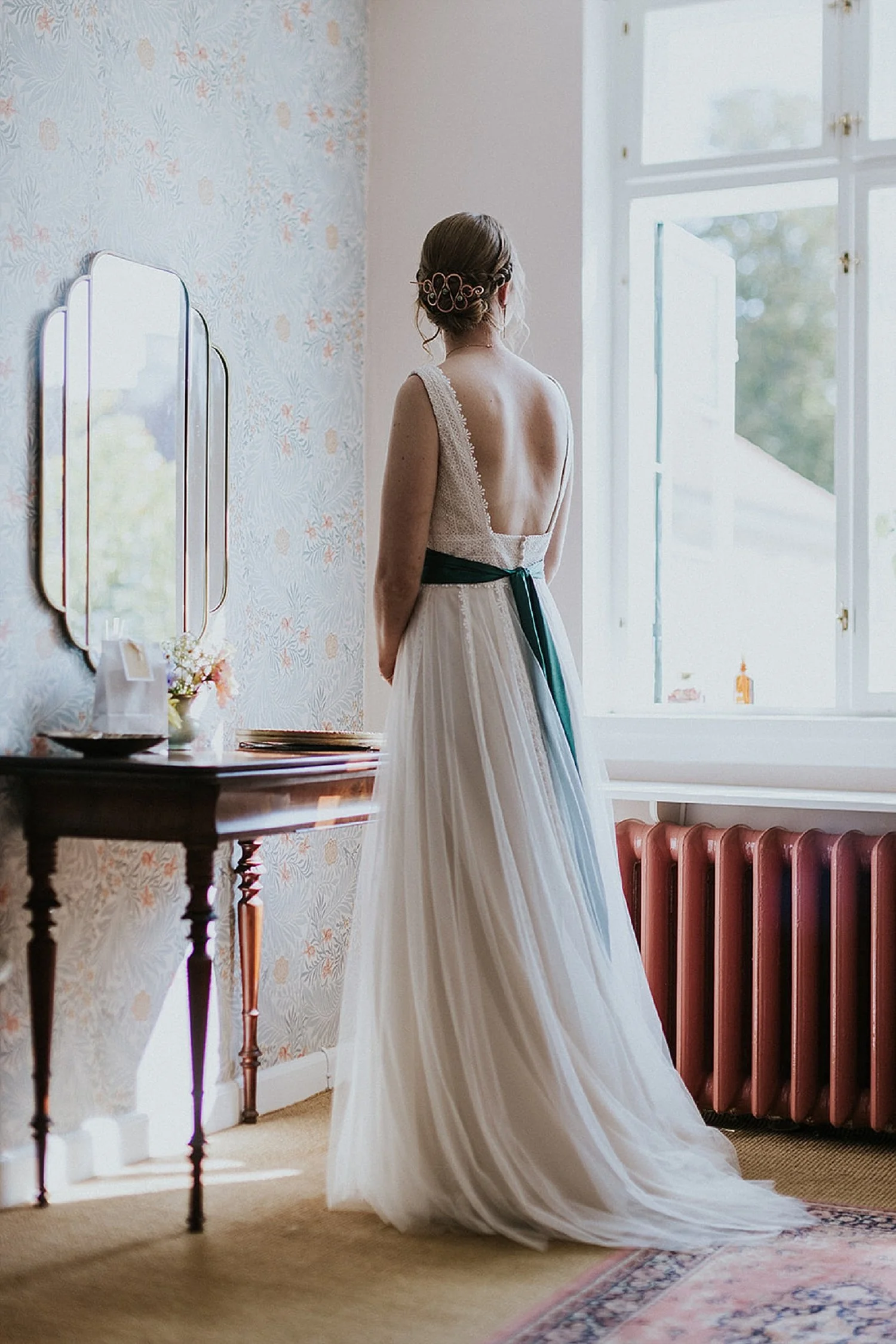 Full length back view of a newly styled bride in front of a mirror wearing a simple elegant wedding dress with a blue ribbon