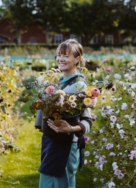 Louise Badino, the founder of Danish Island Weddings, smiling with her arms full of natural island flowers, showcasing her expert skills in crafting wild bridal bouquets and elegant floral arrangements for romantic elopements on Aeroe.