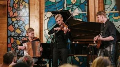 An intimate indoor classical concert inside the wood-paneled music room at Soebygaard. Showcasing a performance with a grand piano beneath vibrant historic glass mosaic artwork on Aeroe Island in Denmark.