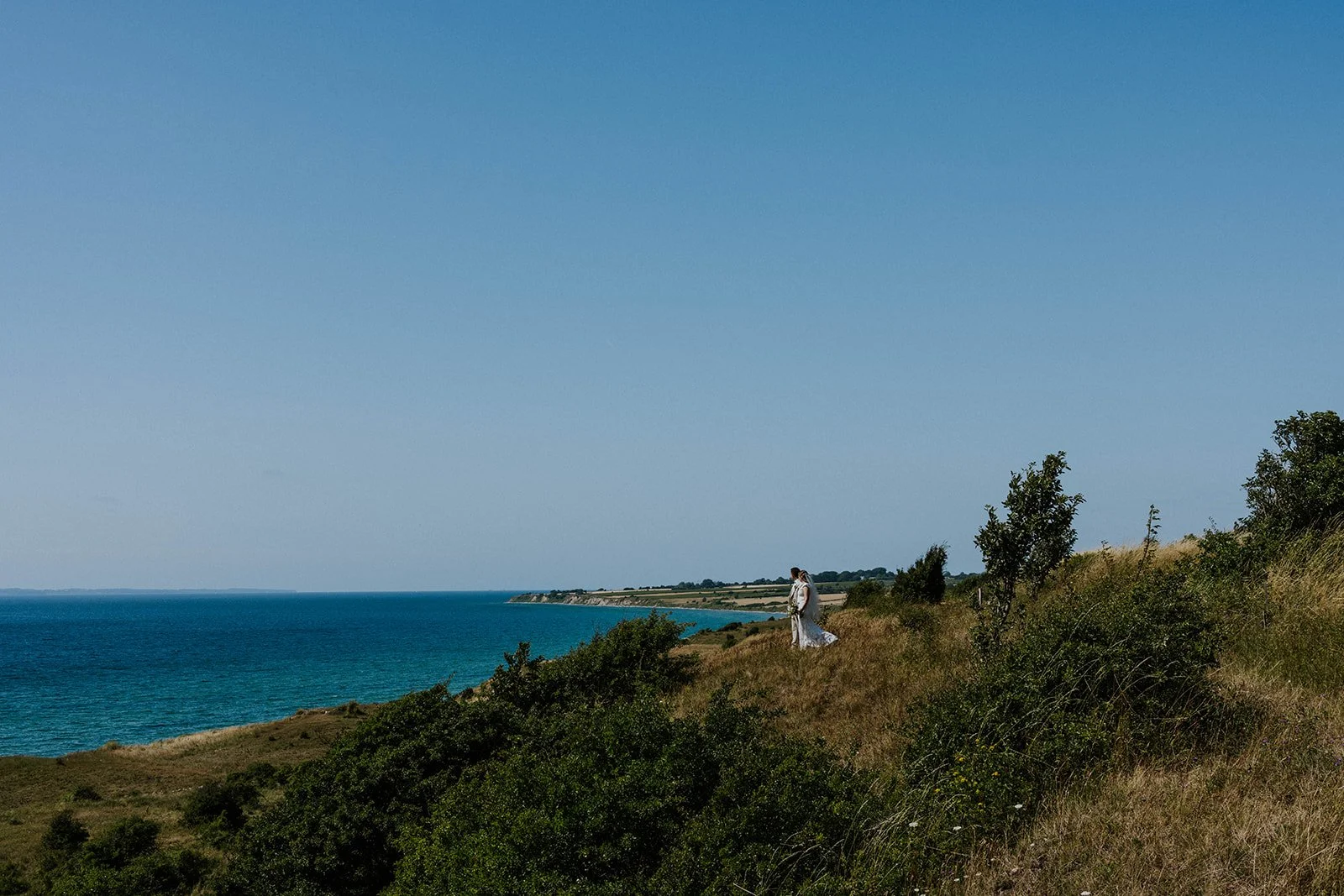 A wedding couple standing on the scenic cliffs of Voderup Klint overlooking the Baltic Sea. An iconic outdoor location for an elopement on Aeroe Island in Denmark.