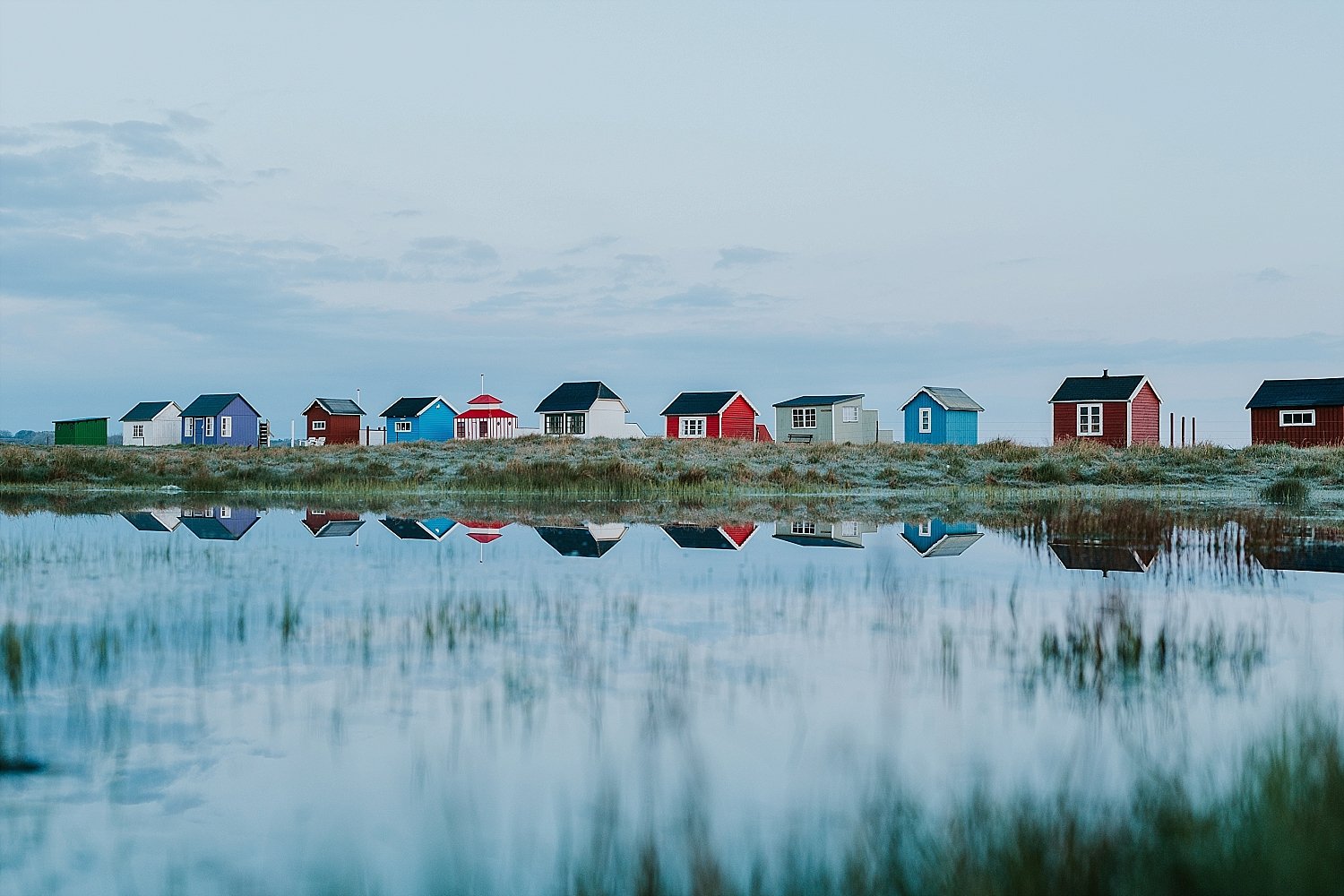 A panoramic view of the iconic colorful beach huts at Vesterstrand reflecting in the calm sea on Aeroe Island.