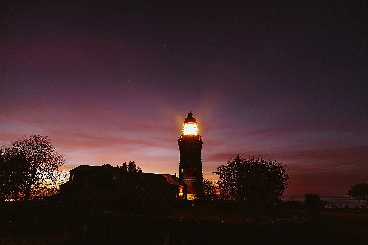 The historic Skjoldnaes Fyr lighthouse illuminated against a deep twilight sky during a dramatic sunset. A romantic coastal landmark for couples celebrating an elopement honeymoon on Aeroe Island in Denmark.