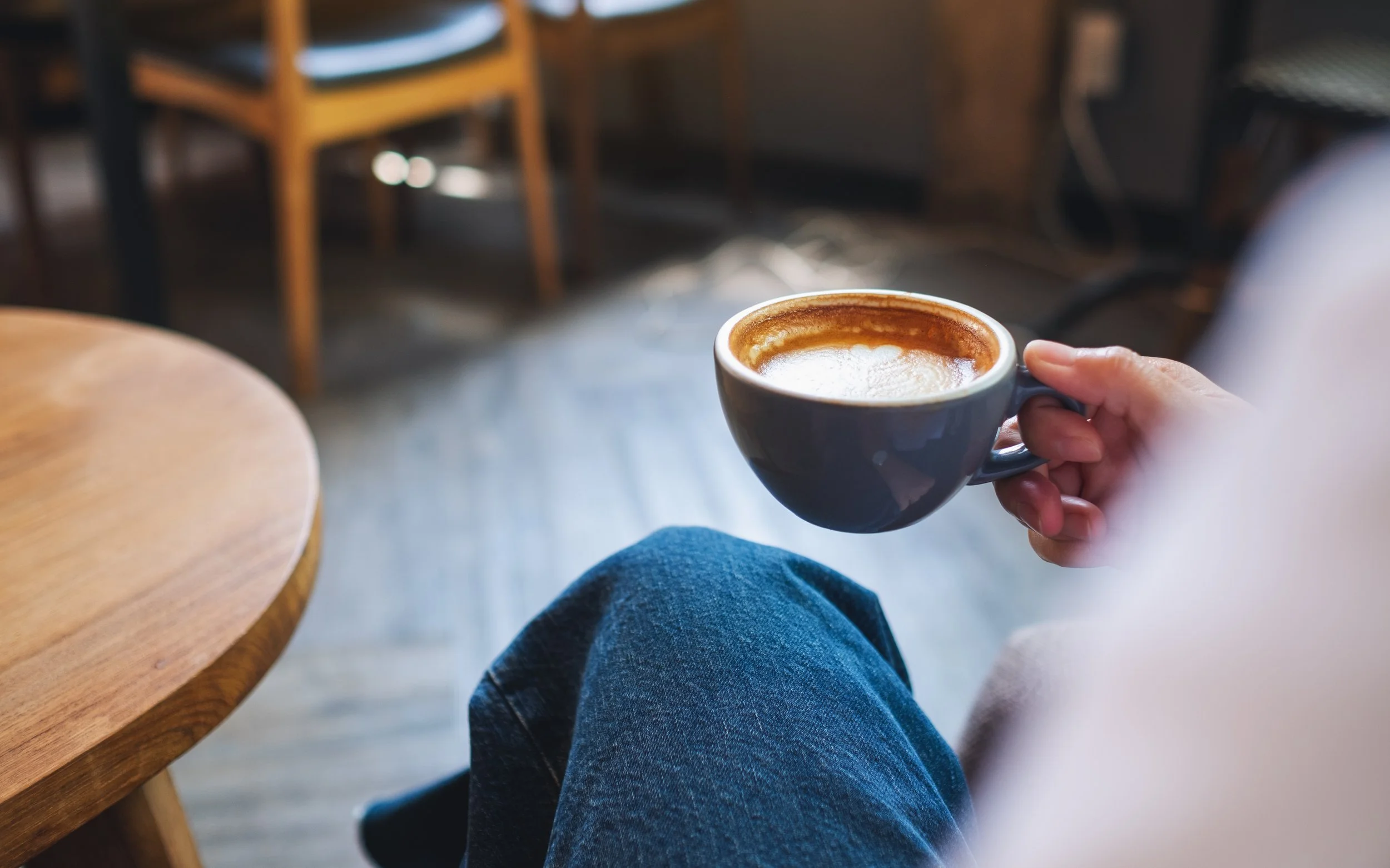 A close-up of a person holding a freshly brewed cup of coffee inside a cozy cafe setting. Perfect lifestyle inspiration for a slow morning during an elopement honeymoon getaway on Aeroe Island in Denmark.