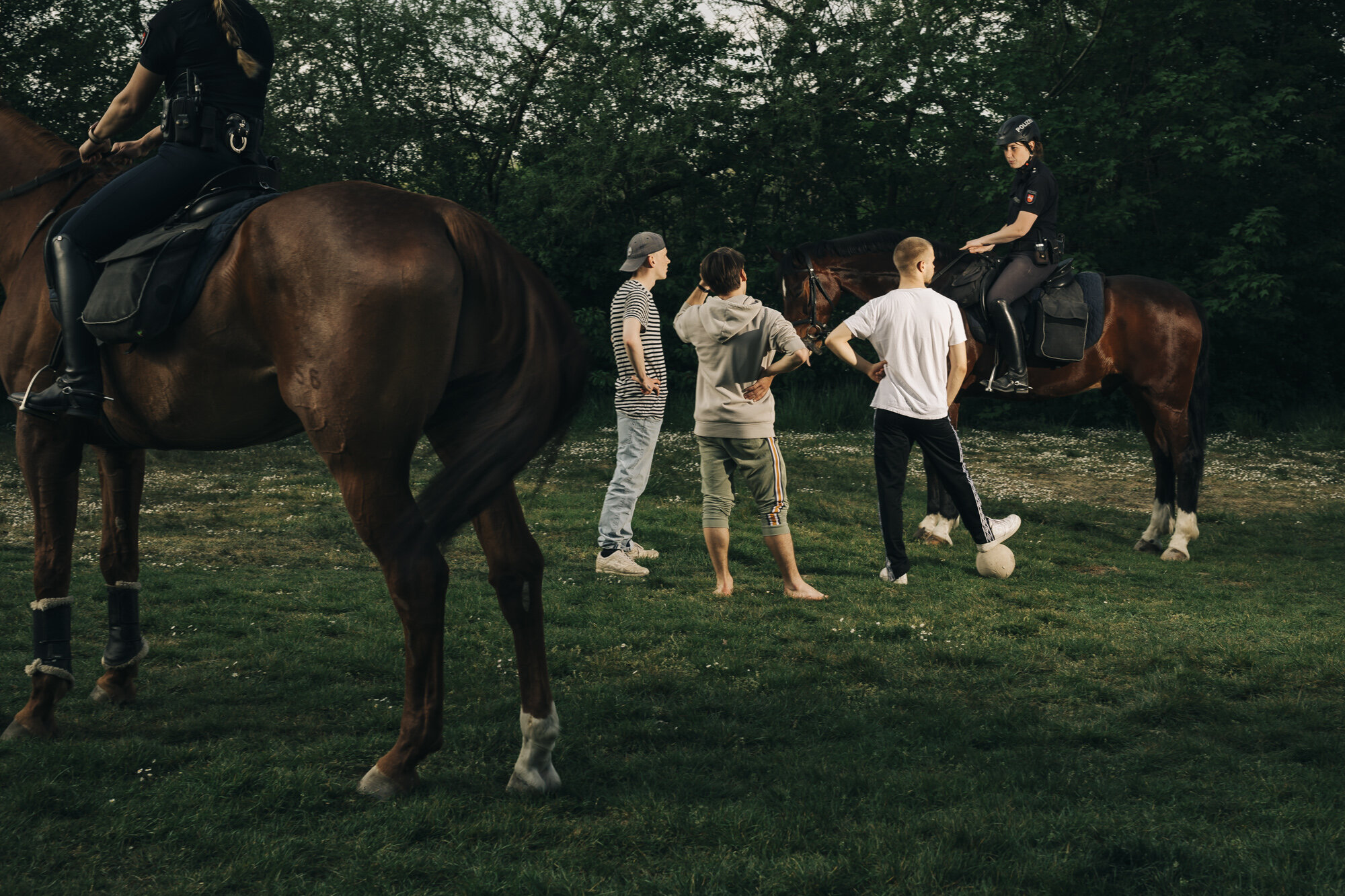  Mounted policewomen disperse three young men playing football in a park. In Germany it is forbidden at the time to be in public with more than two people if you do not belong to a family living in the same household. 