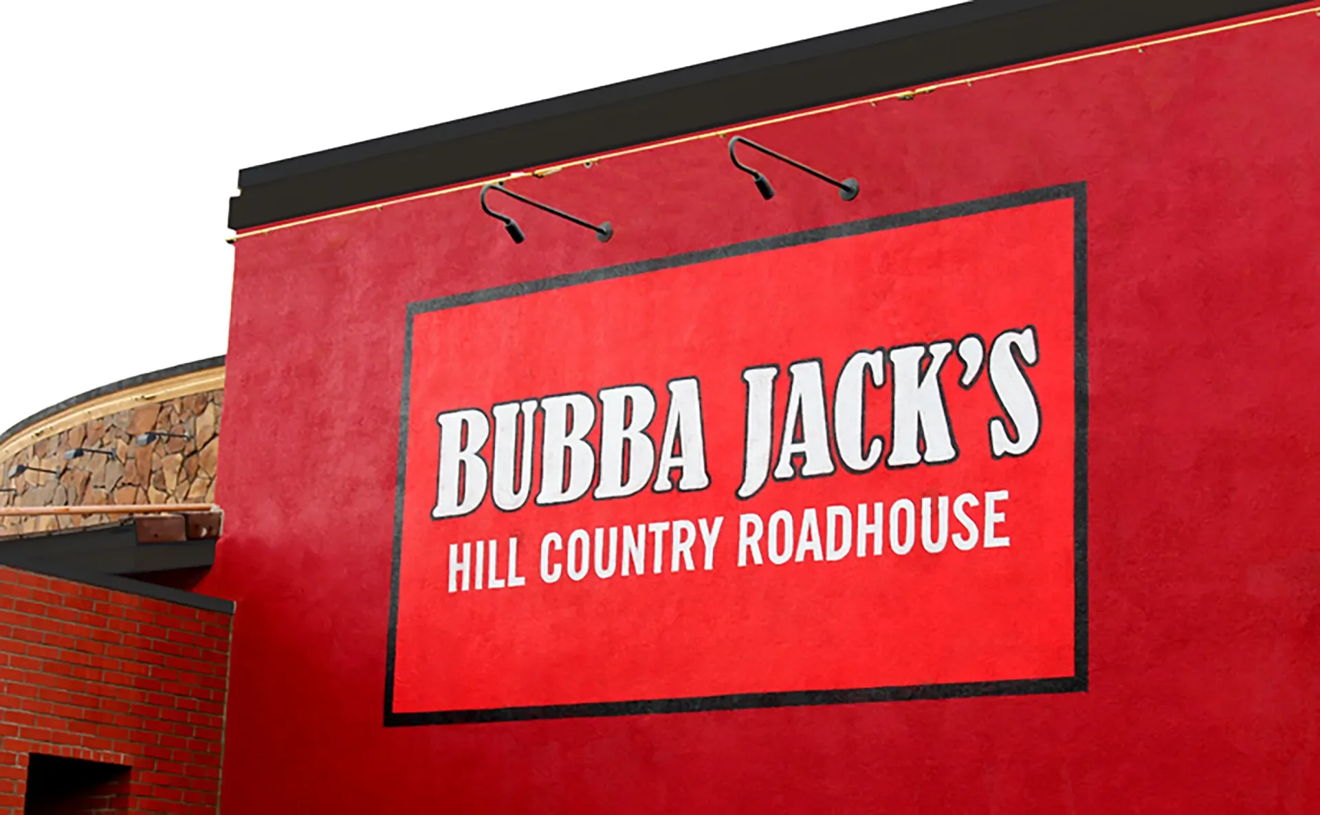 Sign for Bubba Jack's Hill Country Roadhouse on red wall with black border and two black lights above.