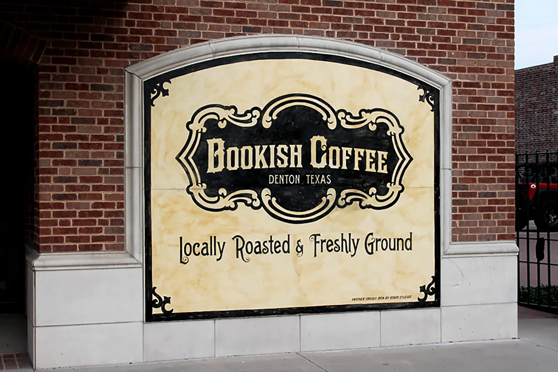 Sign for Bookish Coffee in Denton, Texas, with the tagline 'Locally Roasted & Freshly Ground' on a brick wall.