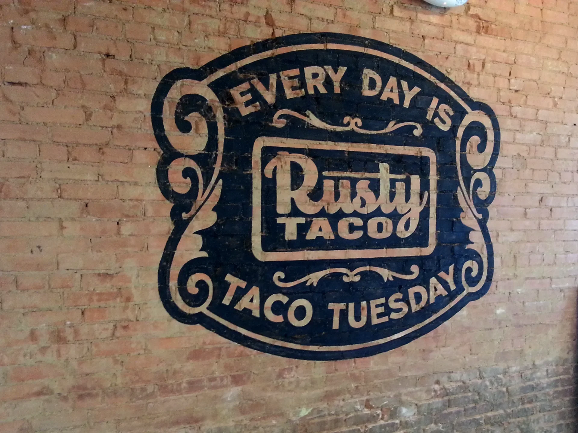 Wall art with the text 'Every day is Taco Tuesday' above a logo that reads 'Rusty Taco' on a brick wall.