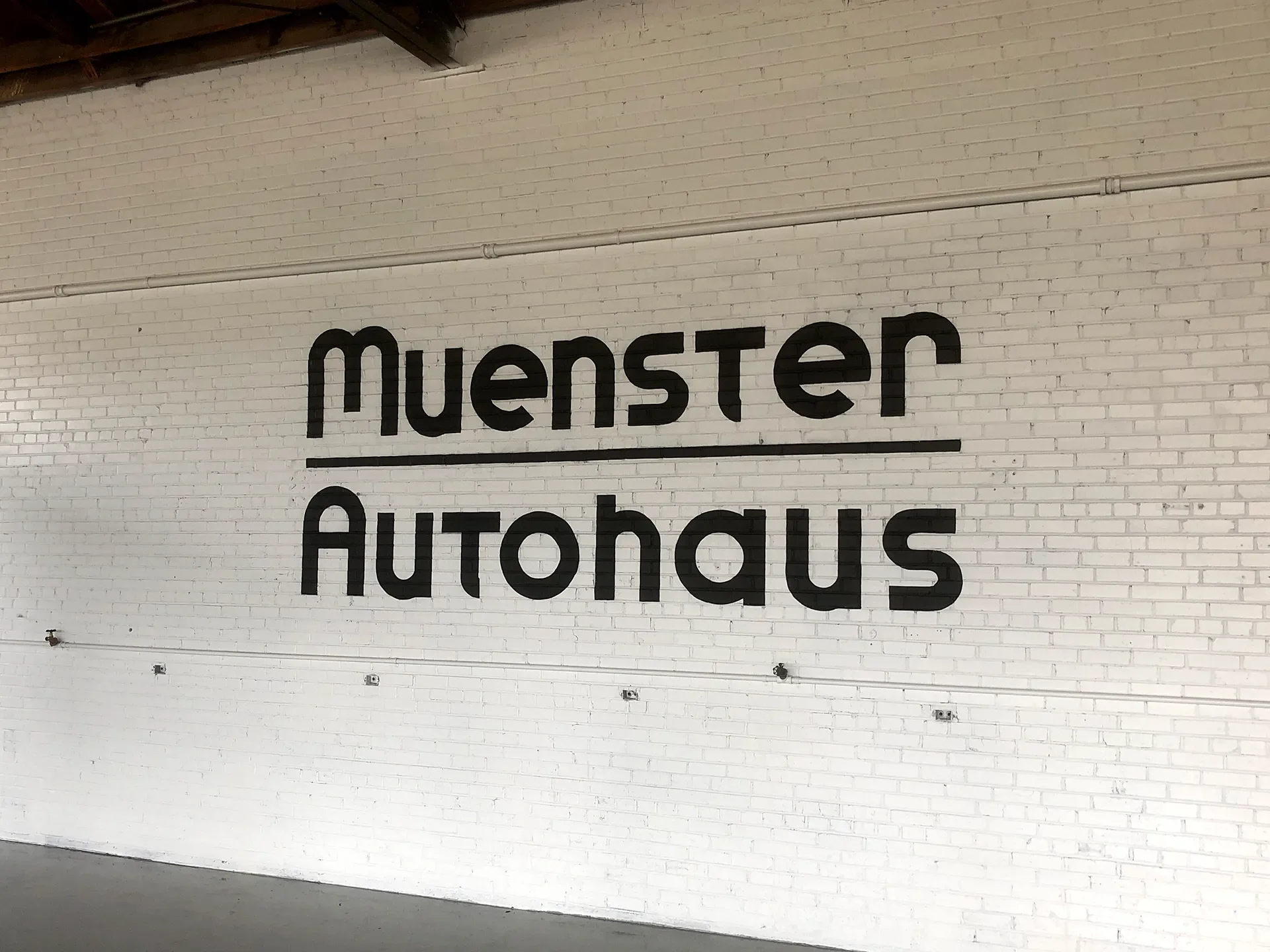 Sign on a white brick wall reading 'Muenster Autohaus' in black letters.