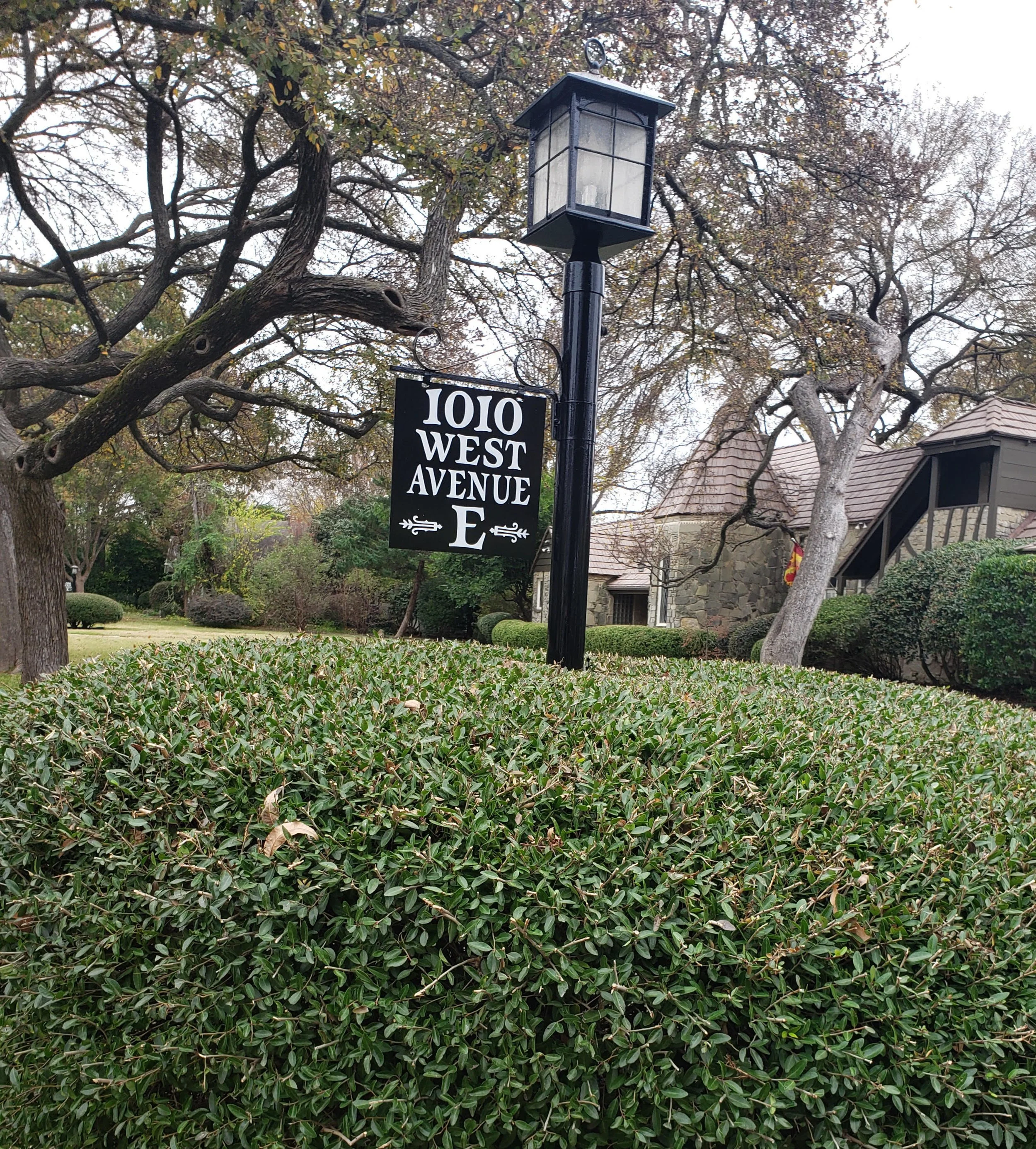 Street sign indicating 1010 West Avenue E, with a lamp post and trees in a residential neighborhood.
