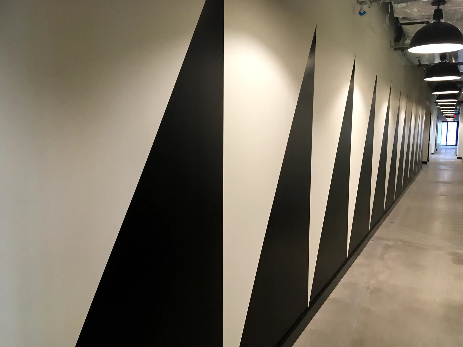 A long hallway with beige flooring and a black and white geometric mural on the wall featuring large black triangles and white spaces.