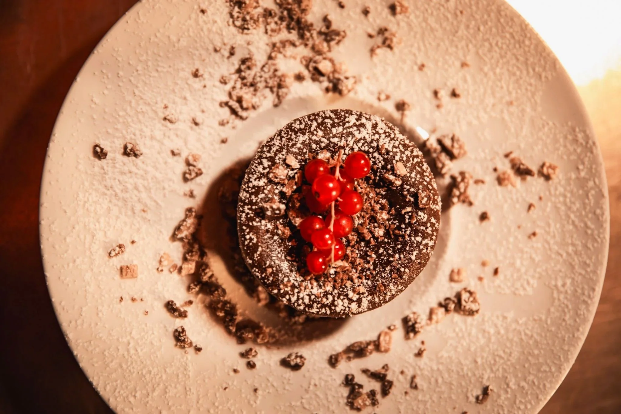 Un dessert chocolaté décoré avec des groseilles rouges, saupoudré de cacao, présenté sur une assiette blanche.
