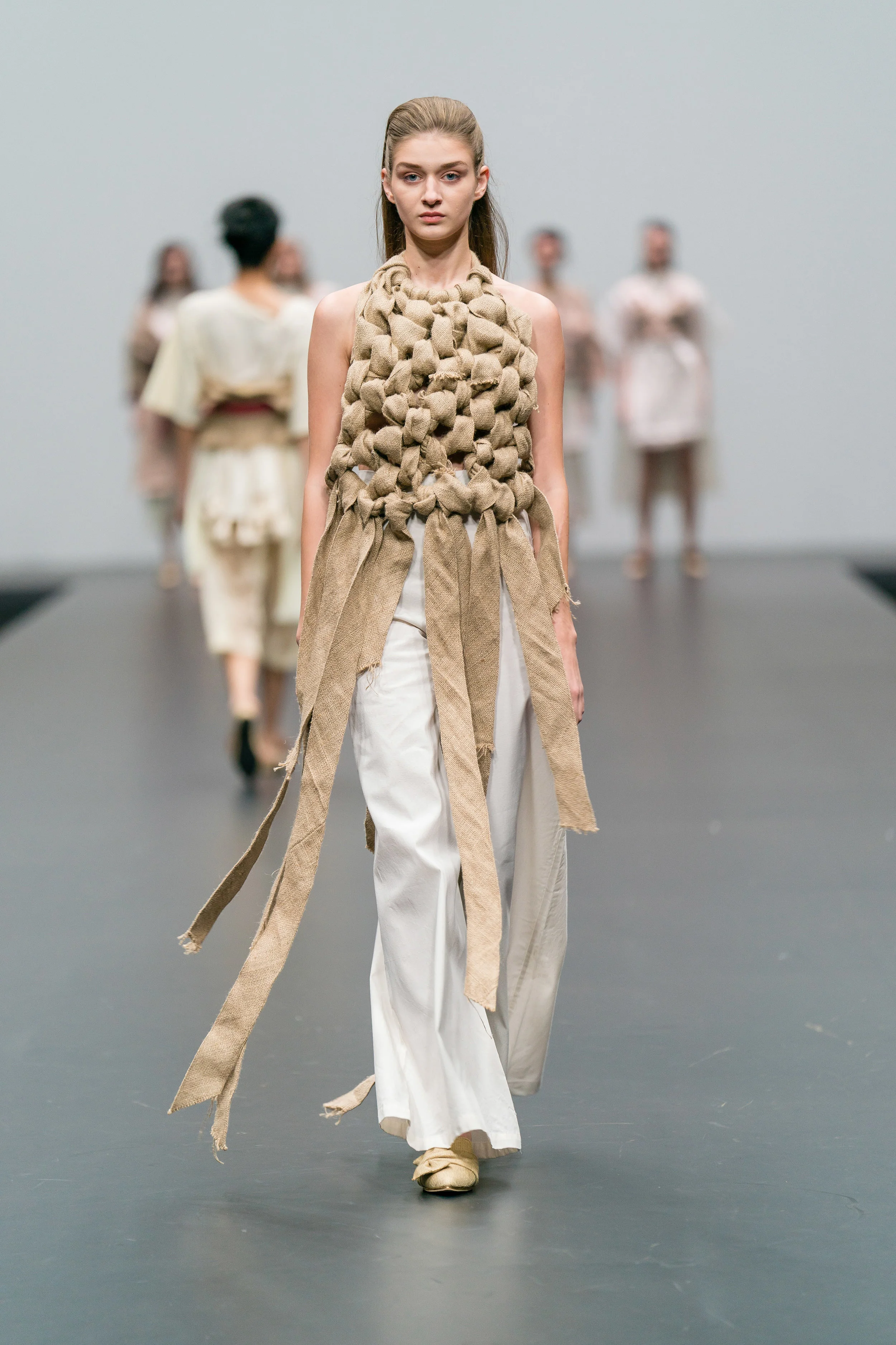 Sarah Devina Susanto Up-cycled oversized knot halterneck made from jute sacks, and white oversized trousers made from secondhand textiles 