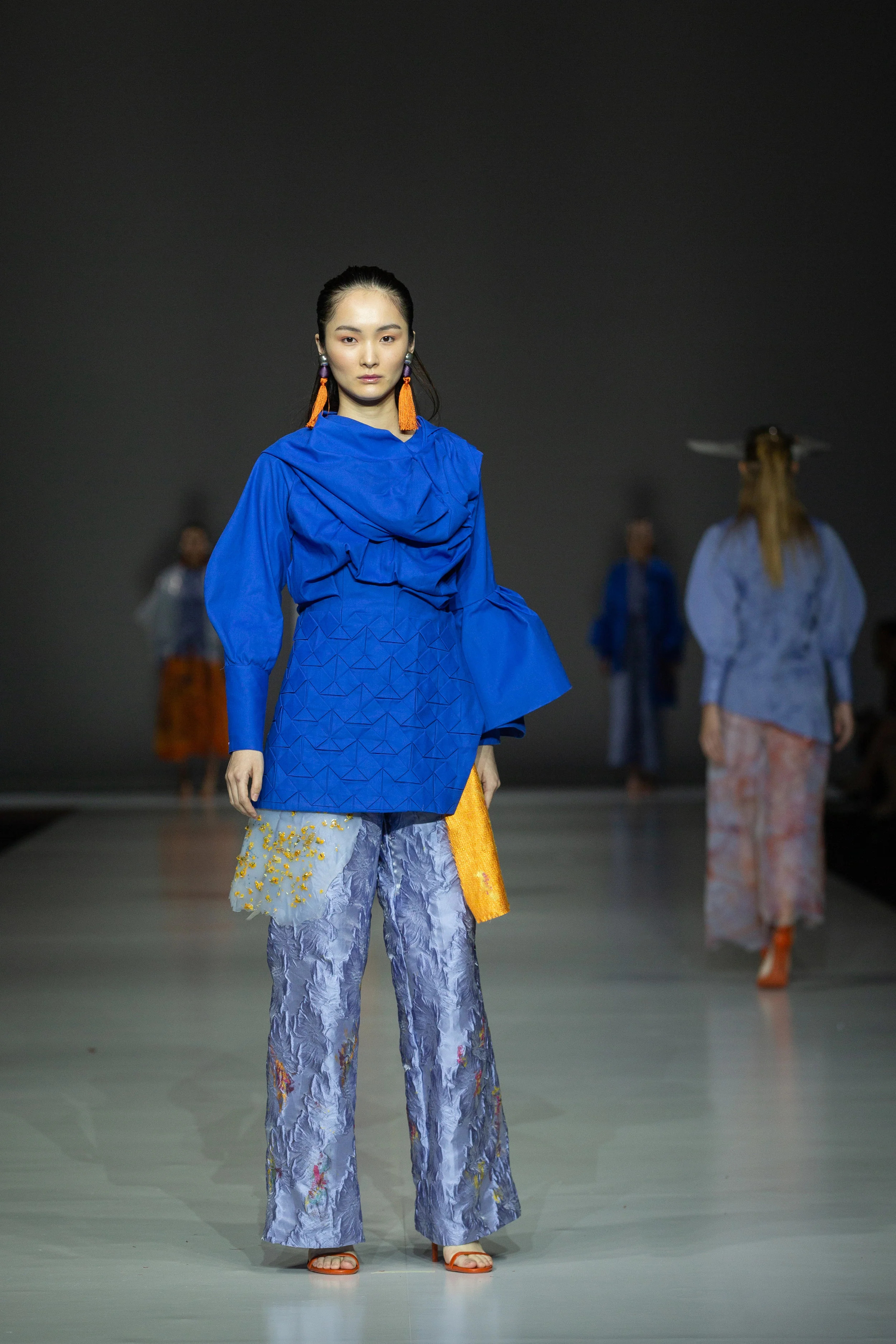 Lucia Alcaina Zero-waste draped blue top with structured origami detailing made from up-cycled cut-and-sew waste, damaged textiles and textile scraps, paired with up-cycled brocade trousers with silicone over-skirt, embellished with embroidery and hand-painting