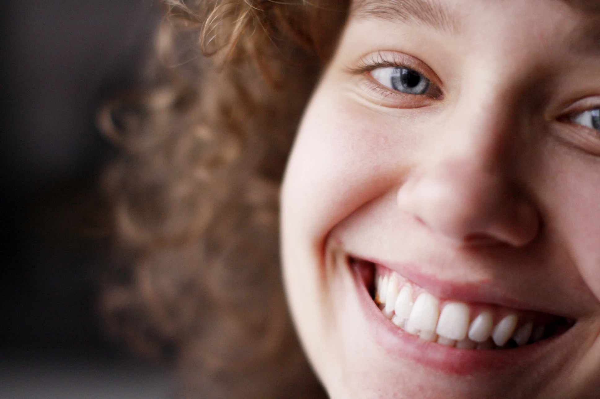 Close-up of a smiling young woman with blue eyes, light skin, and curly hair, showing her teeth.