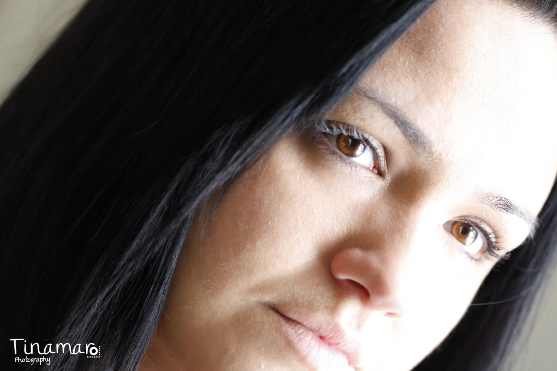 Close-up of a woman with dark hair and brown eyes looking to the side with a slight smile.