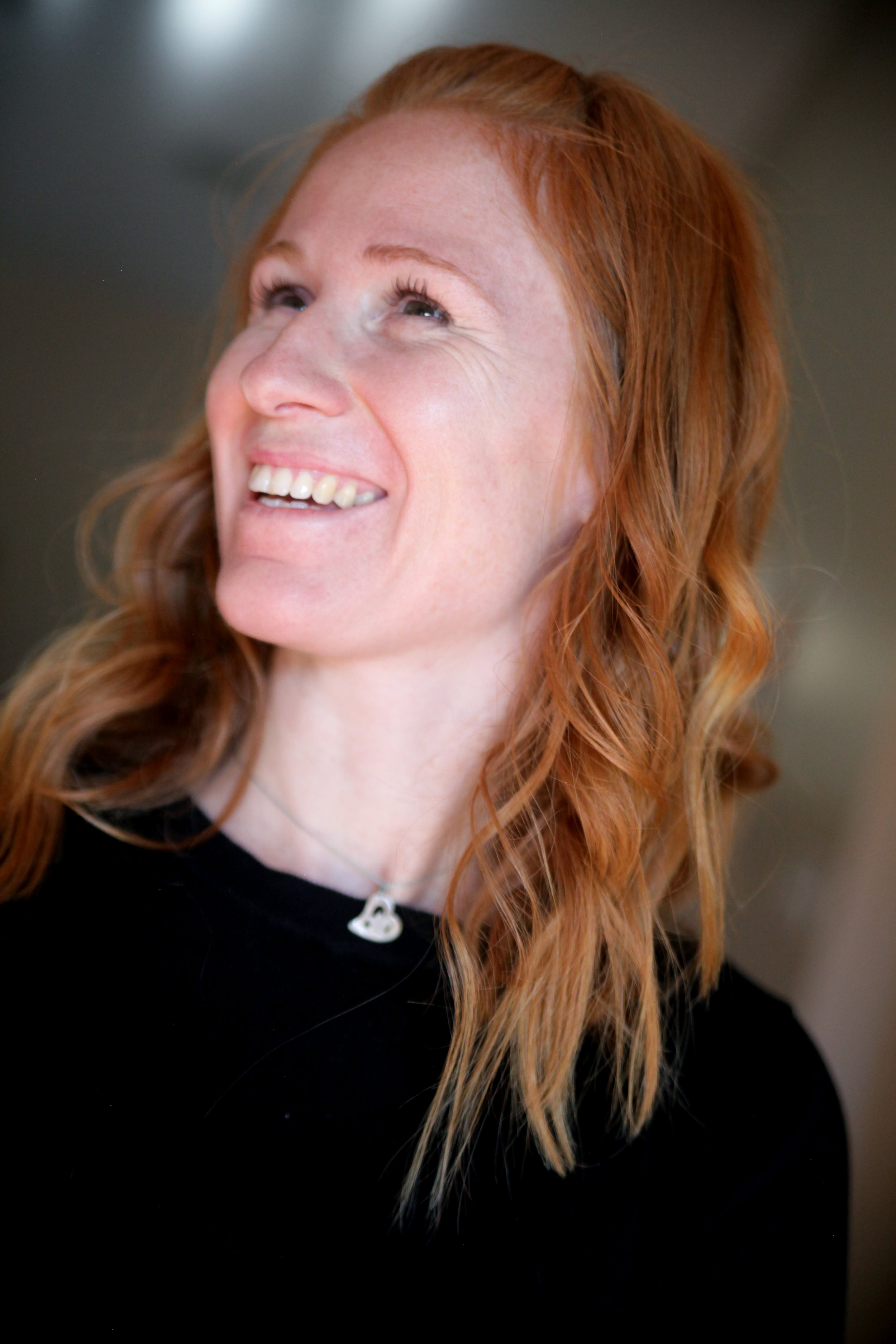 A woman with long, wavy red hair smiling and looking upward.
