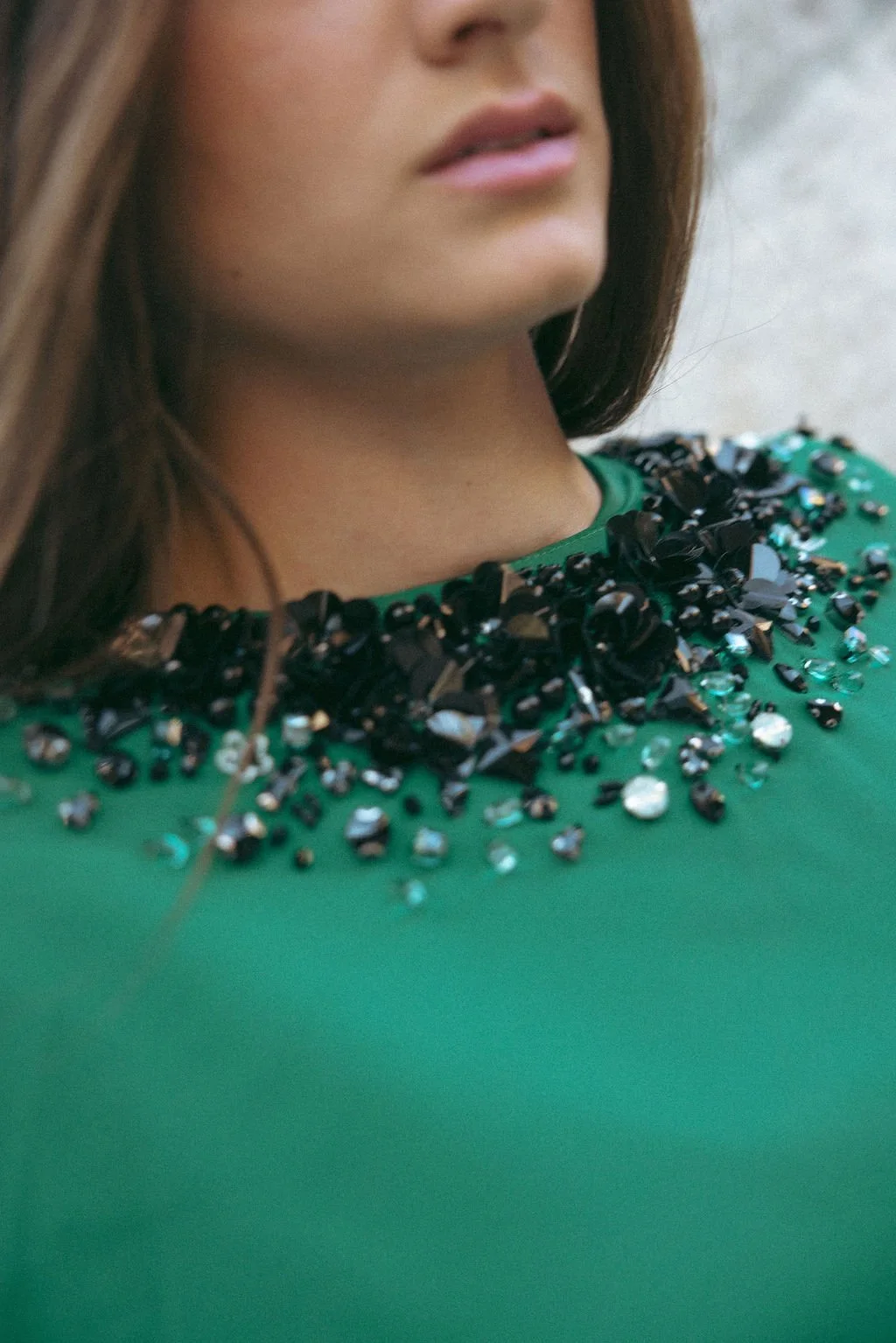 Close-up of a woman wearing a green top with black and reflective embellishments around the neckline.