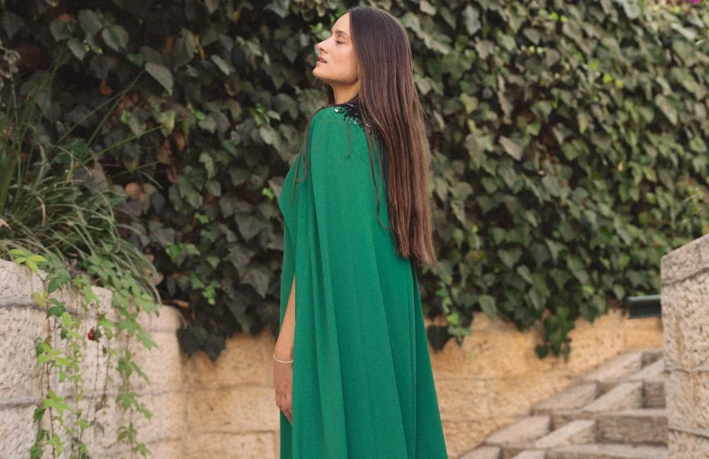 A woman in a green dress standing outdoors near stone steps and bushes.