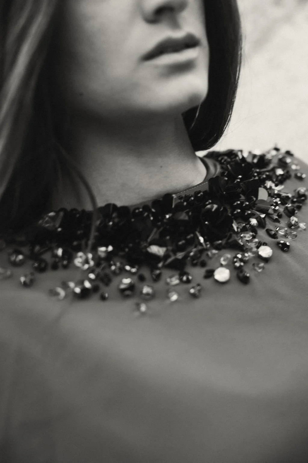 Close-up of woman's face and neck, with focus on her lips and a beaded necklace with large, shiny black and clear stones.