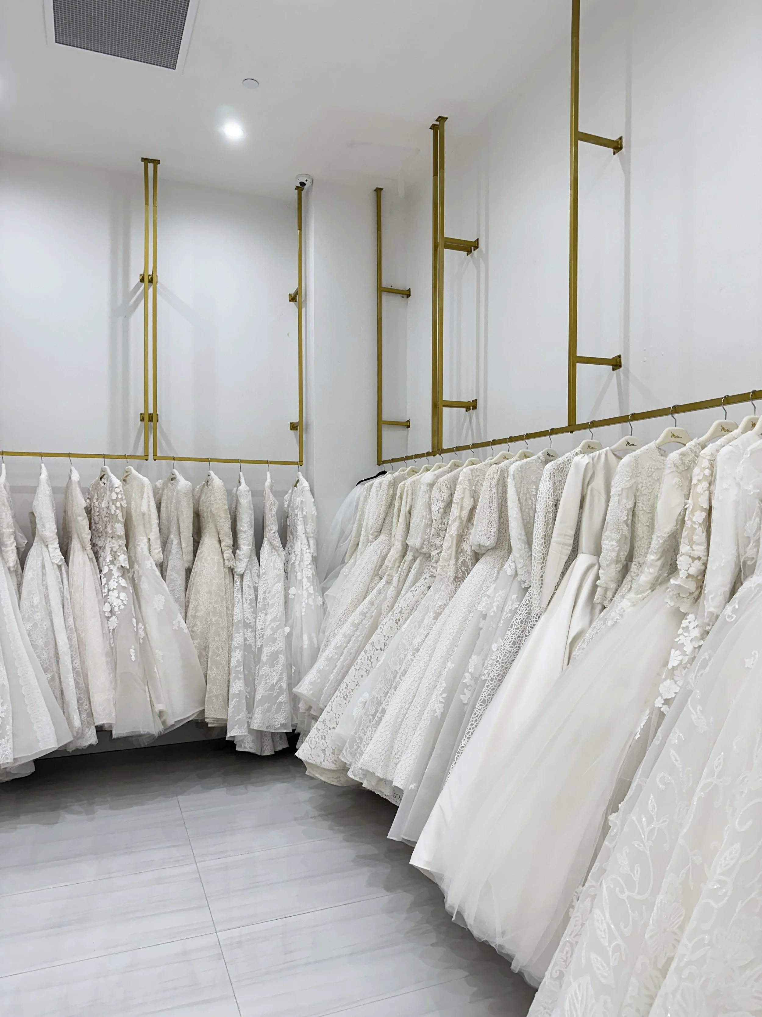 Cream-colored wedding dresses with lace and embroidery hanging in a bridal boutique.