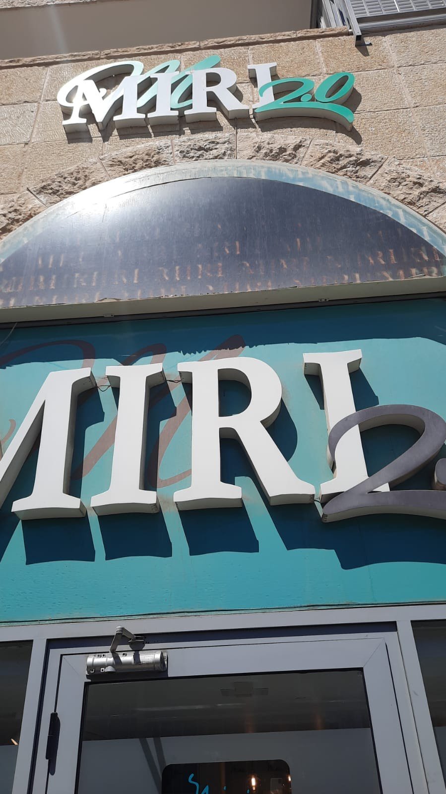 Sign on building reading 'MIR 2' with a blue background and white and gray text, part of a name that likely continues beyond the visible area.