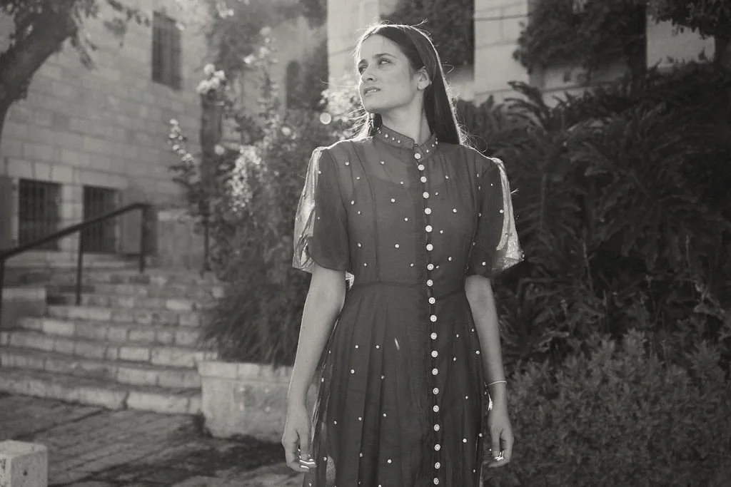 Young woman in a vintage dress standing outdoors with steps and shrubbery in the background