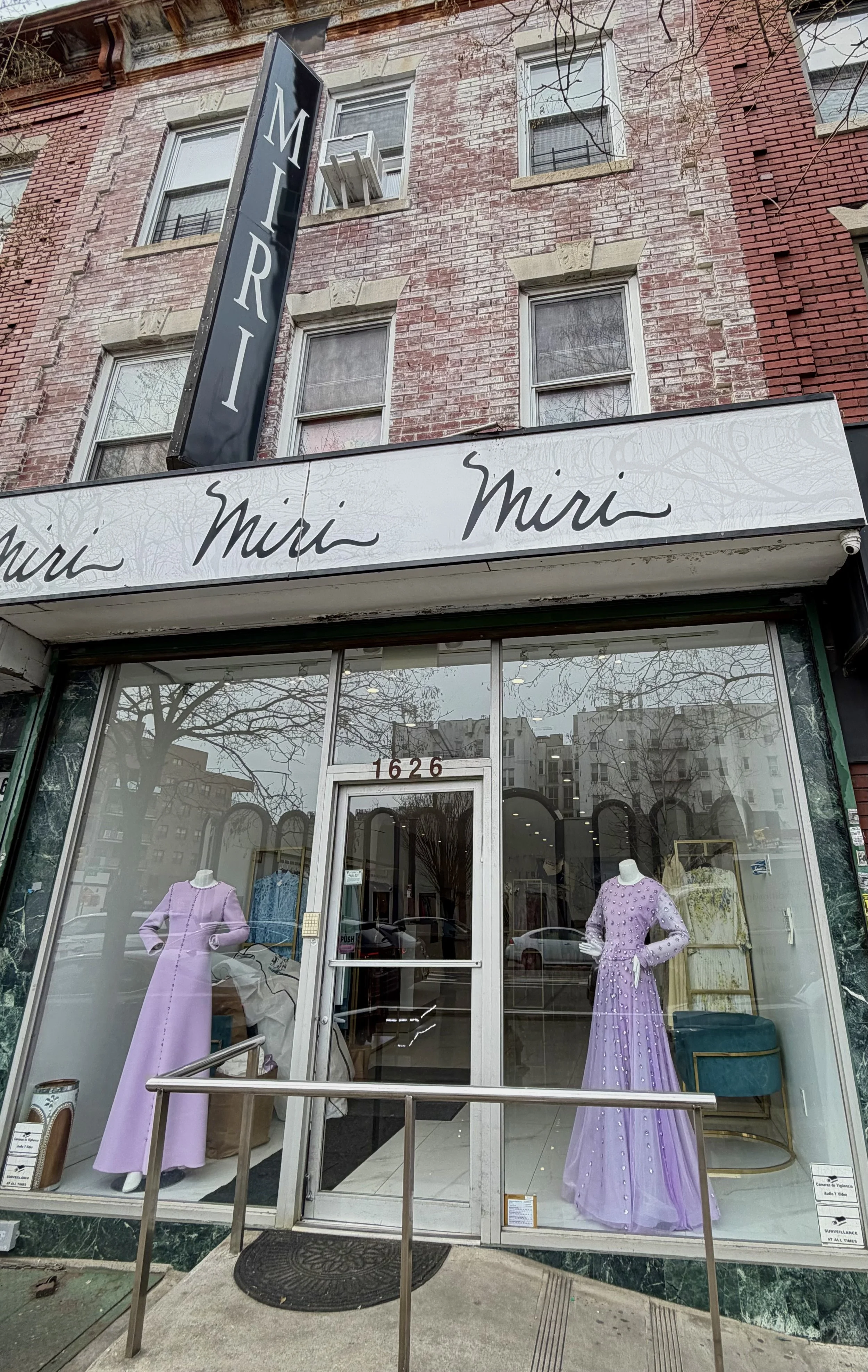 The storefront of Mimi, a clothing boutique, with large windows displaying mannequins dressed in stylish clothing inside. The store is housed in a brick building, and the sign above the entrance reads 'Mimi'.