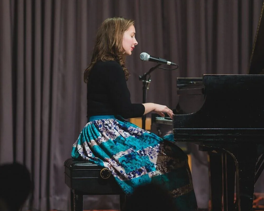 Woman playing piano and singing into a microphone at McAllister Music Studio concert