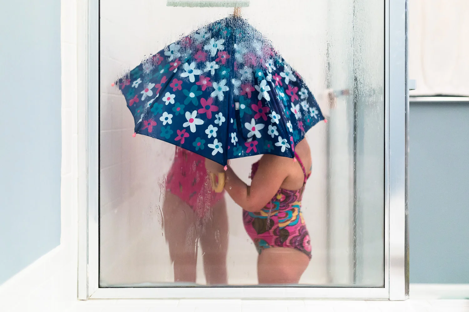 Two kids in shower wearing bathing suits under an umbrella