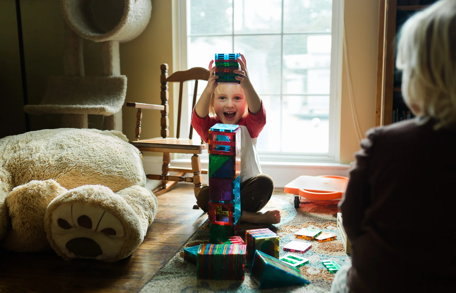 boy building tower of magna tiles with toys on the floor
