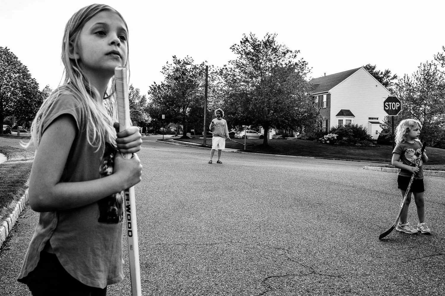 Two girls and dad in street with hockey sticks