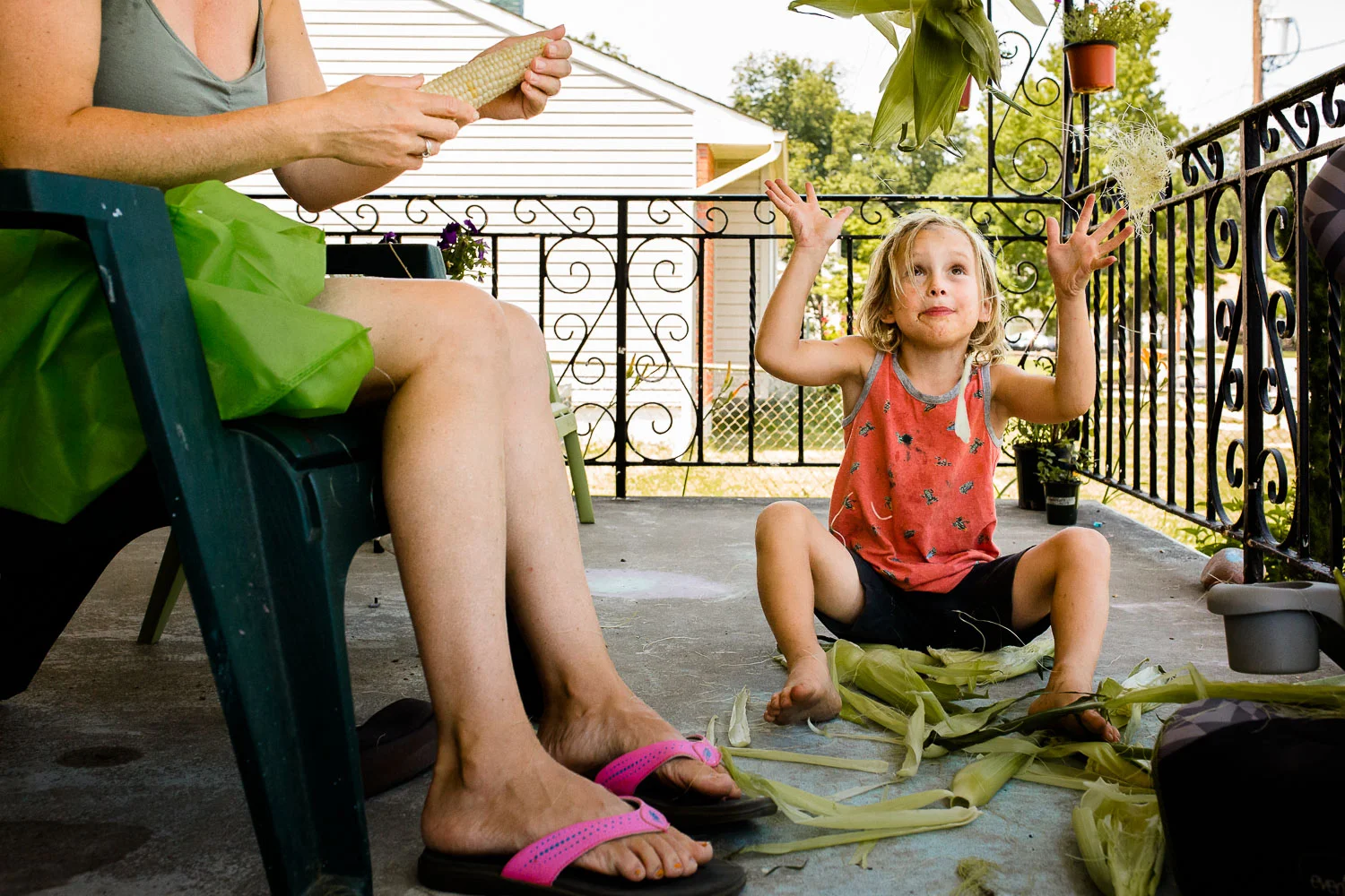 Boy throwing corn husks in the air while sitting on porch with mom.
