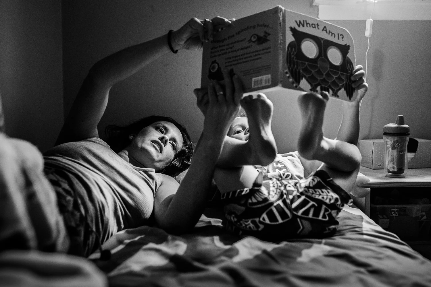 Black and white photo of mom reading to son on bed.