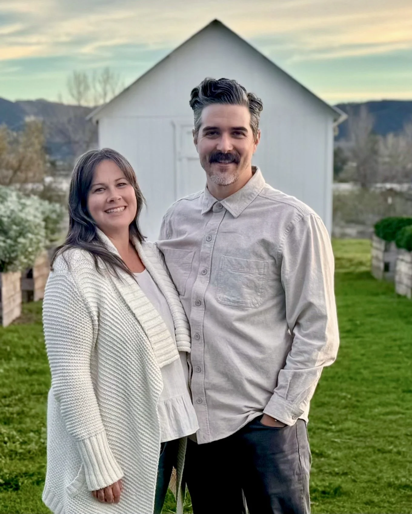 Eldership couple. A smiling couple standing outdoors in front of a white barn and a green lawn during sunset.