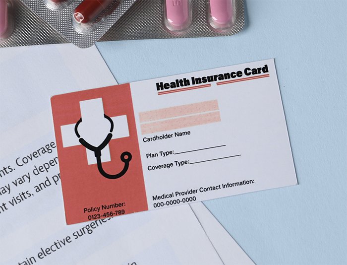Photo of a Health Insurance Card with red accents, paperwork, and pills around it