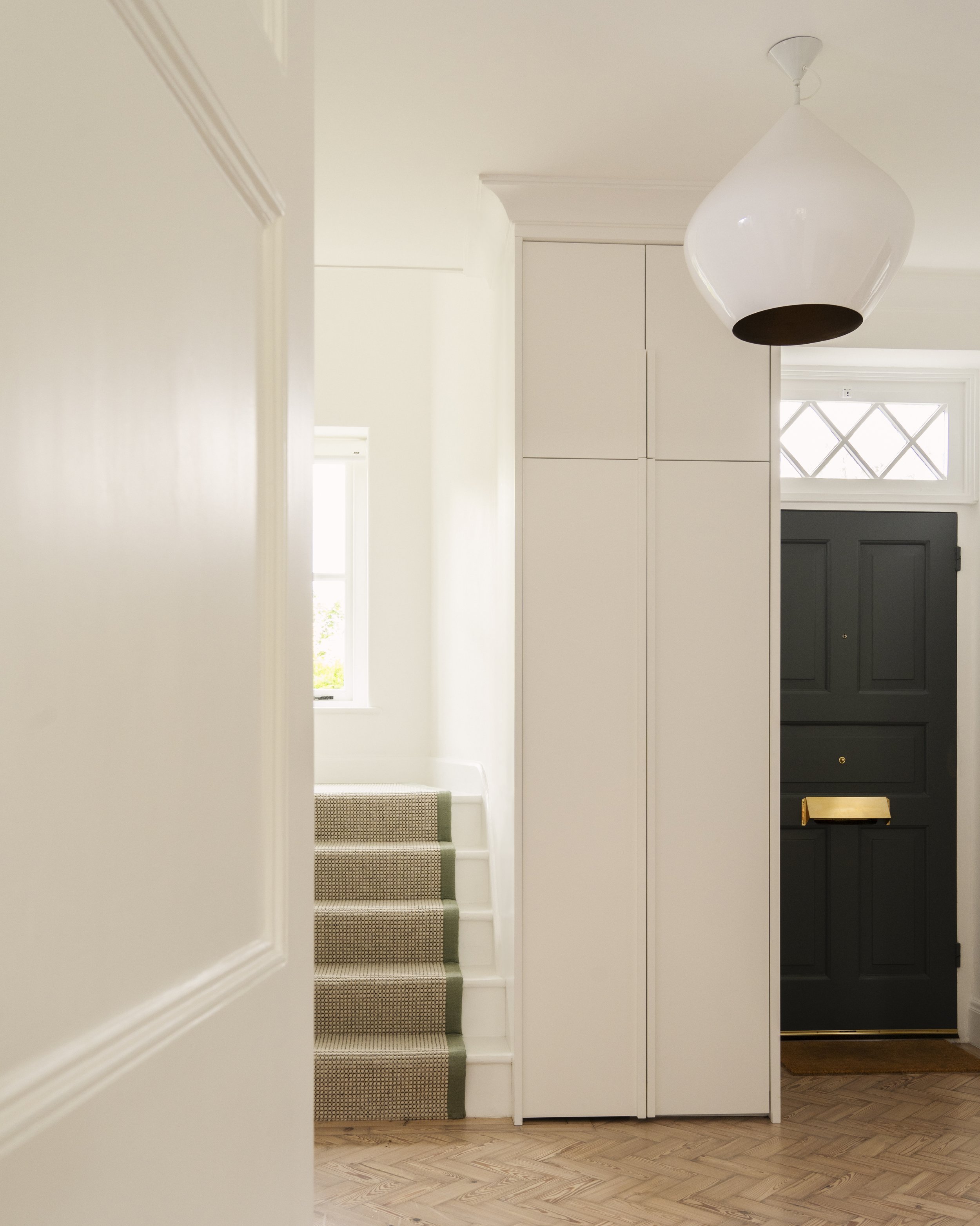Bright hallway with woven stair runner, high white cabinetry and dark green front door.