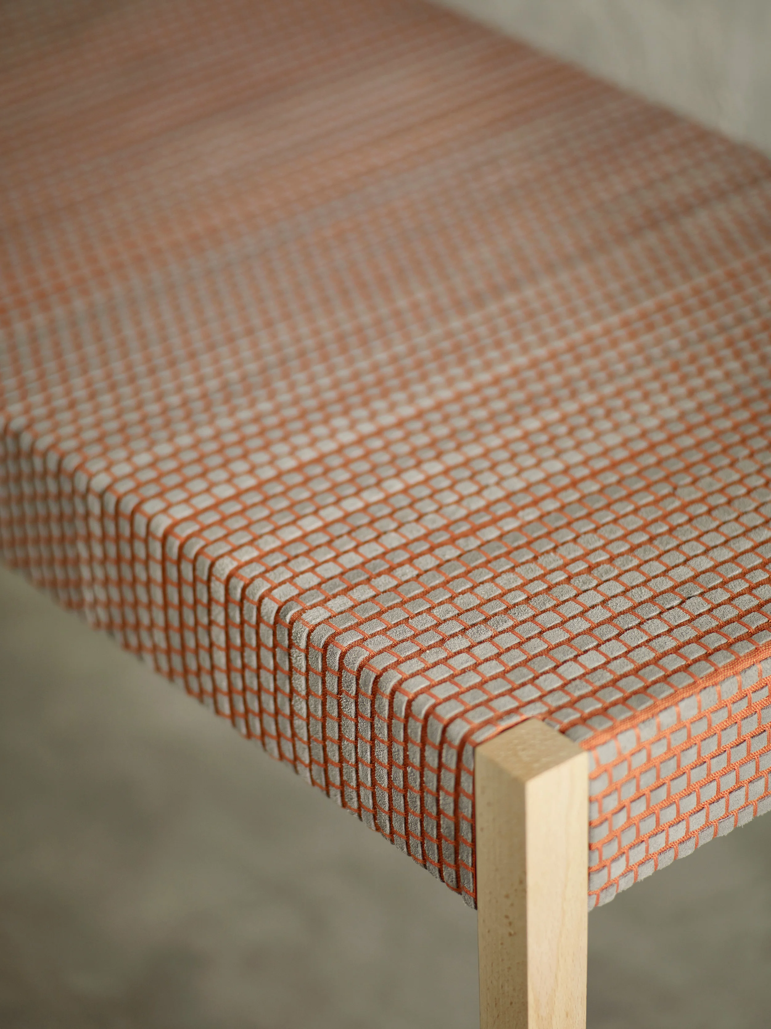 Close-up of bench corner showing tightly upholstered fabric with orange and grey grid pattern over a light wood frame.