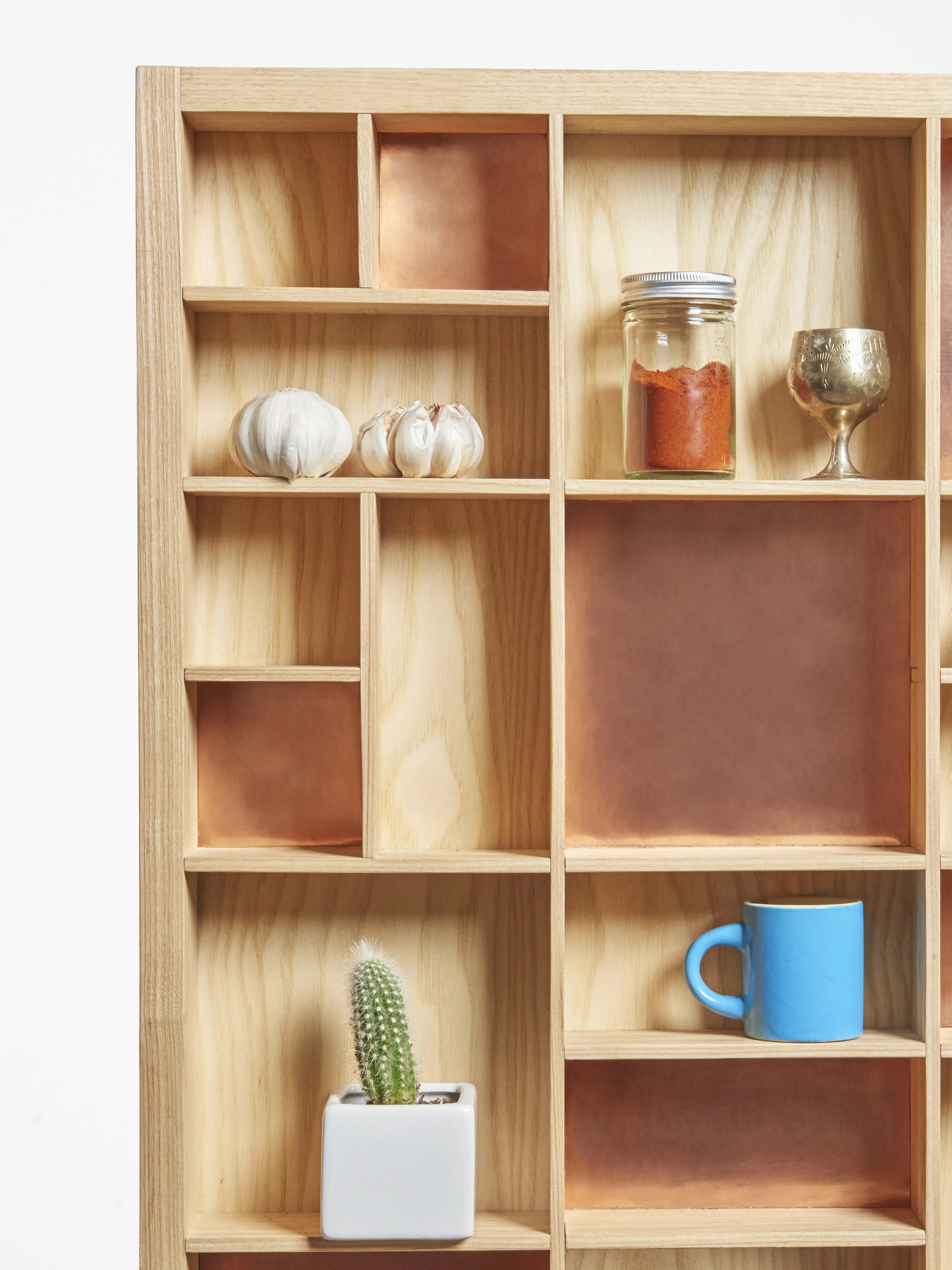 Close-up of the shelf unit with objects such as garlic, a spice jar, a goblet, a cactus in a white pot, and a blue mug.
