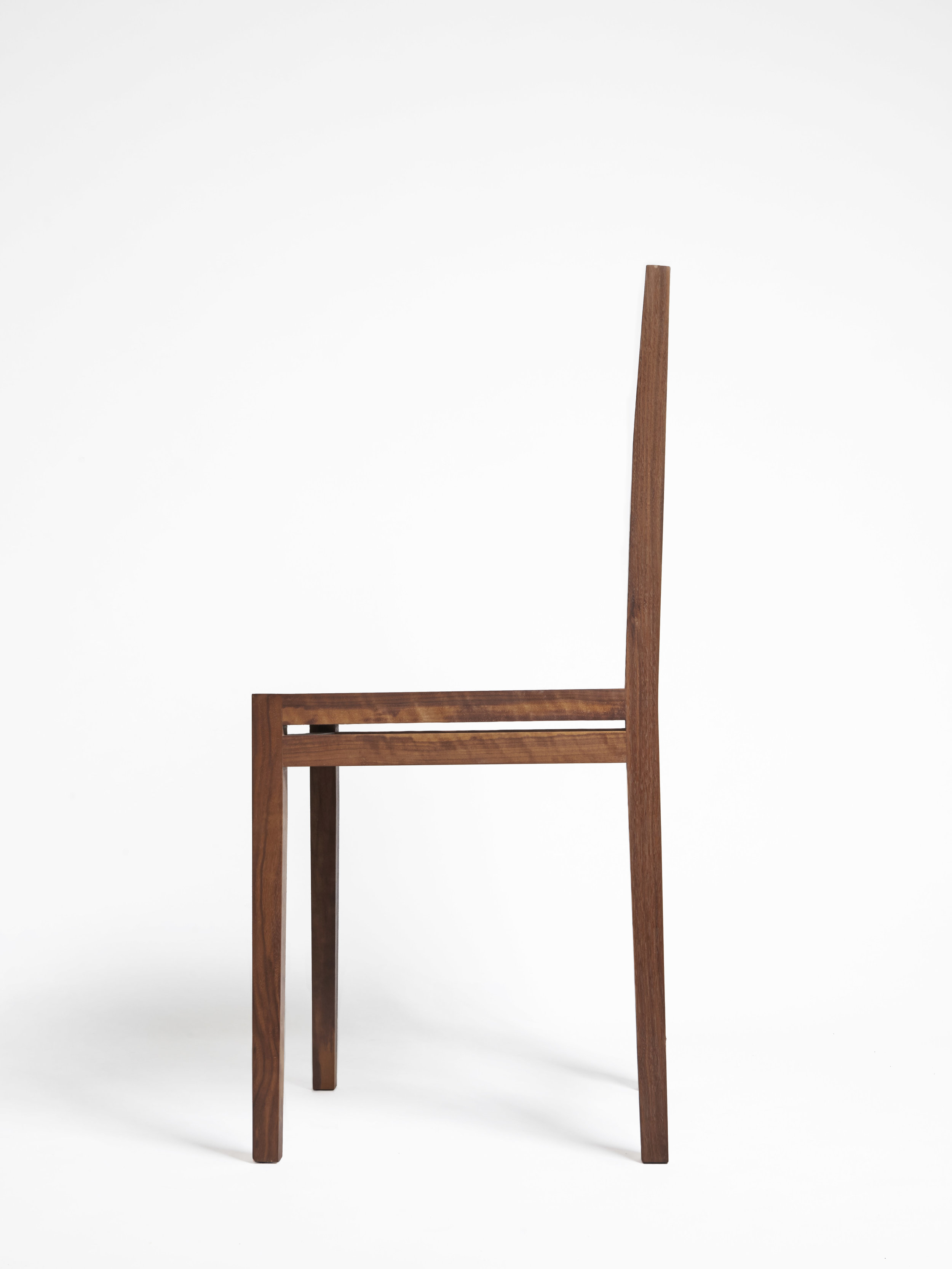 Side profile of a minimalist wooden chair with a tall slatted backrest.