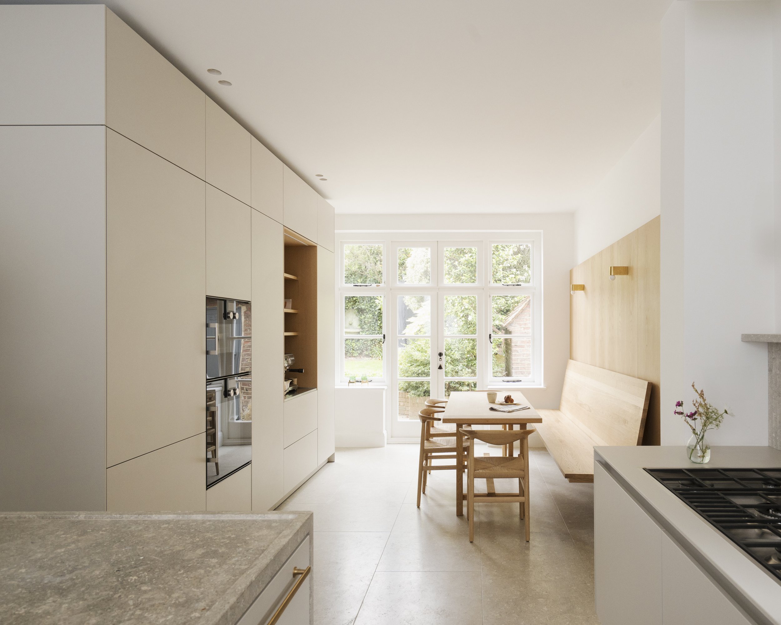 Open-plan kitchen and dining space with built-in cabinetry, wall-hung oak bench and large garden-facing window.
