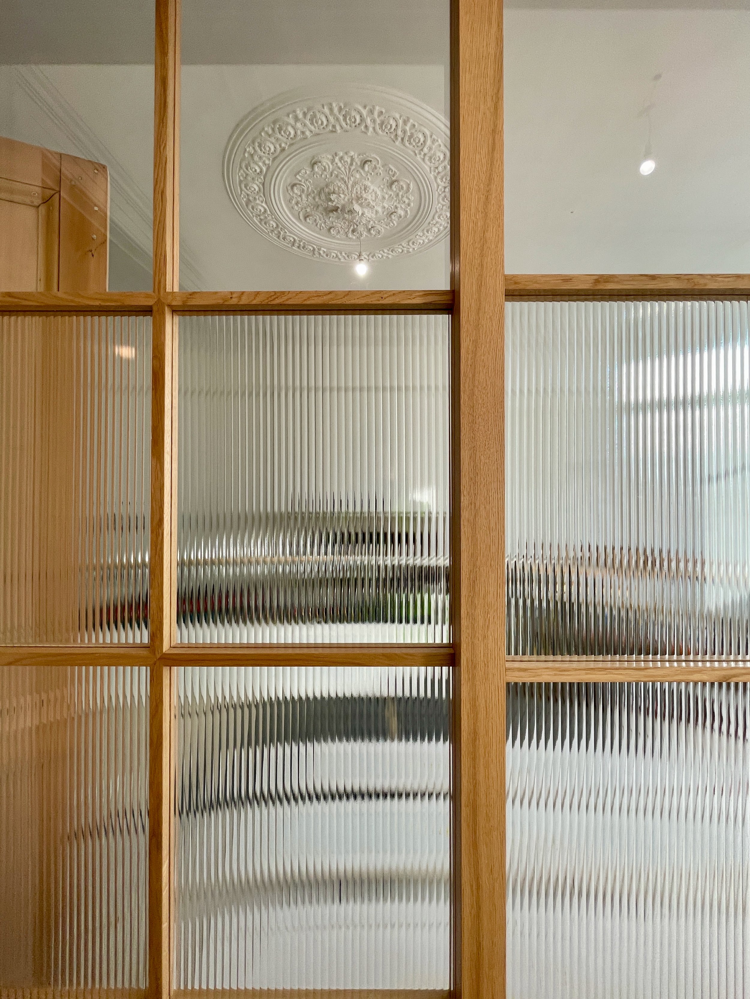 Detail view of a fluted glass sliding door with wooden framing, showing a decorative ceiling rose in the background.