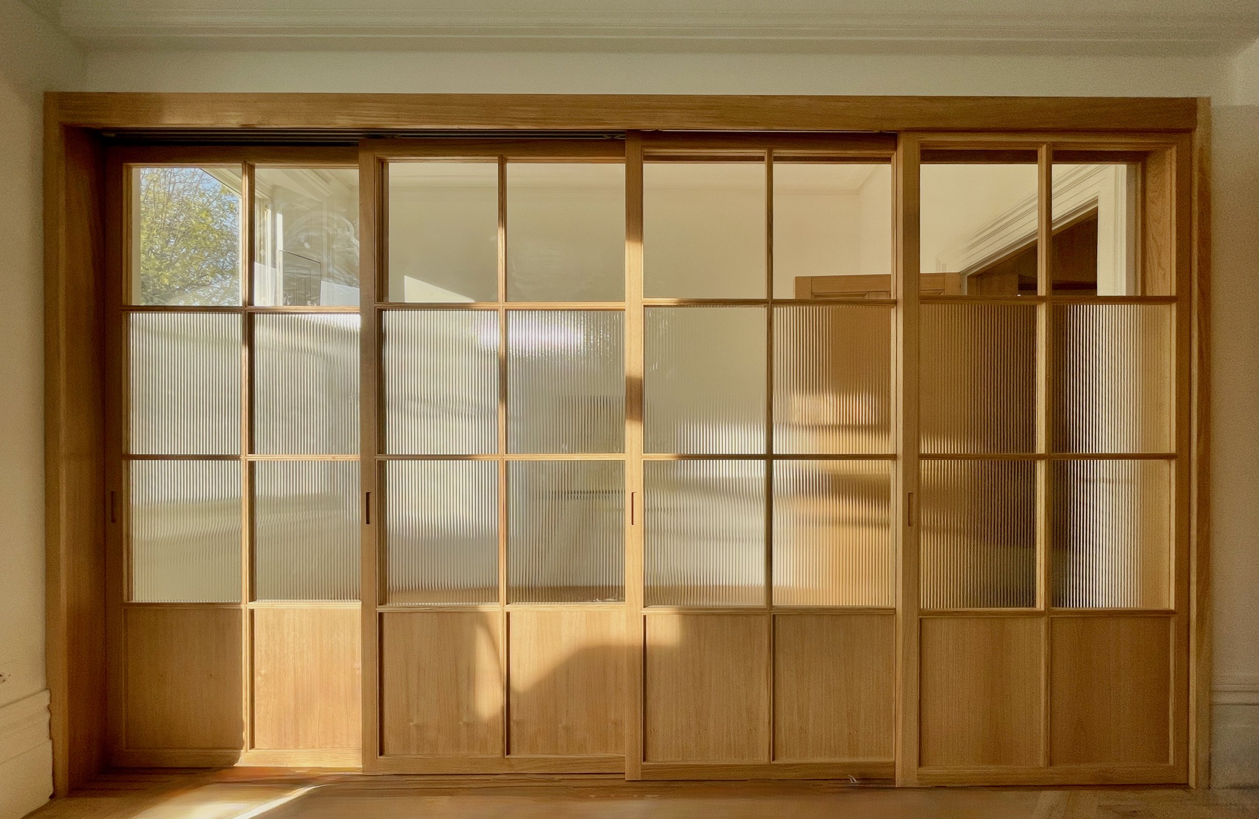 Full front view of closed fluted glass sliding doors in wooden frames, dividing two rooms in a bright interior.