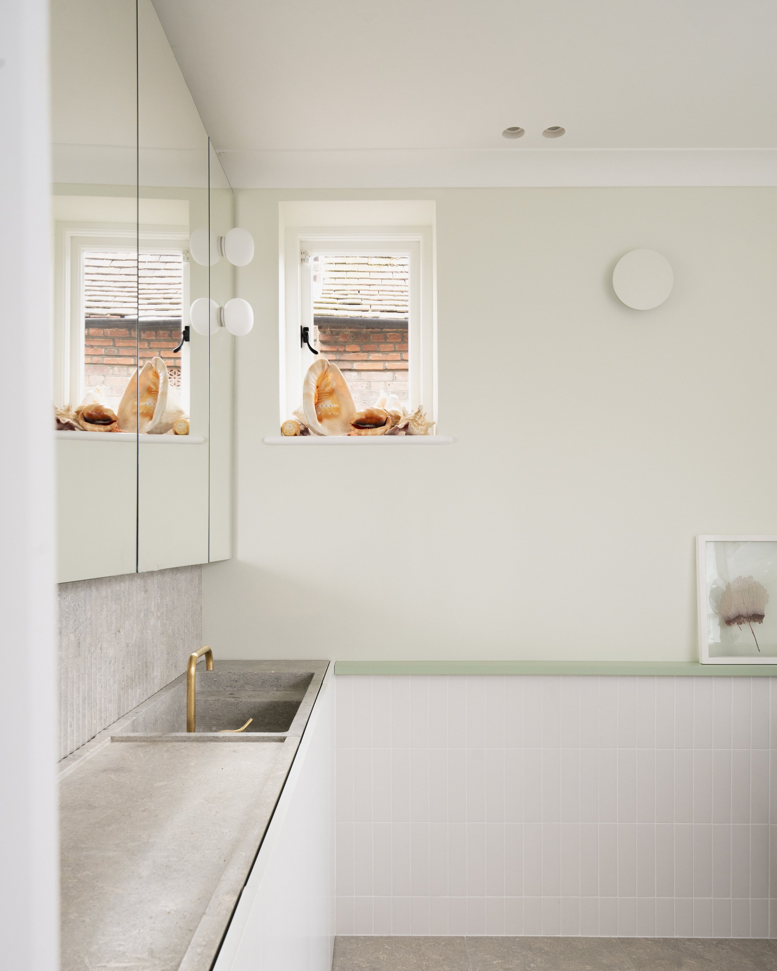 Pale green bathroom with mirrored cabinets, seashell display and reeded concrete backsplash.