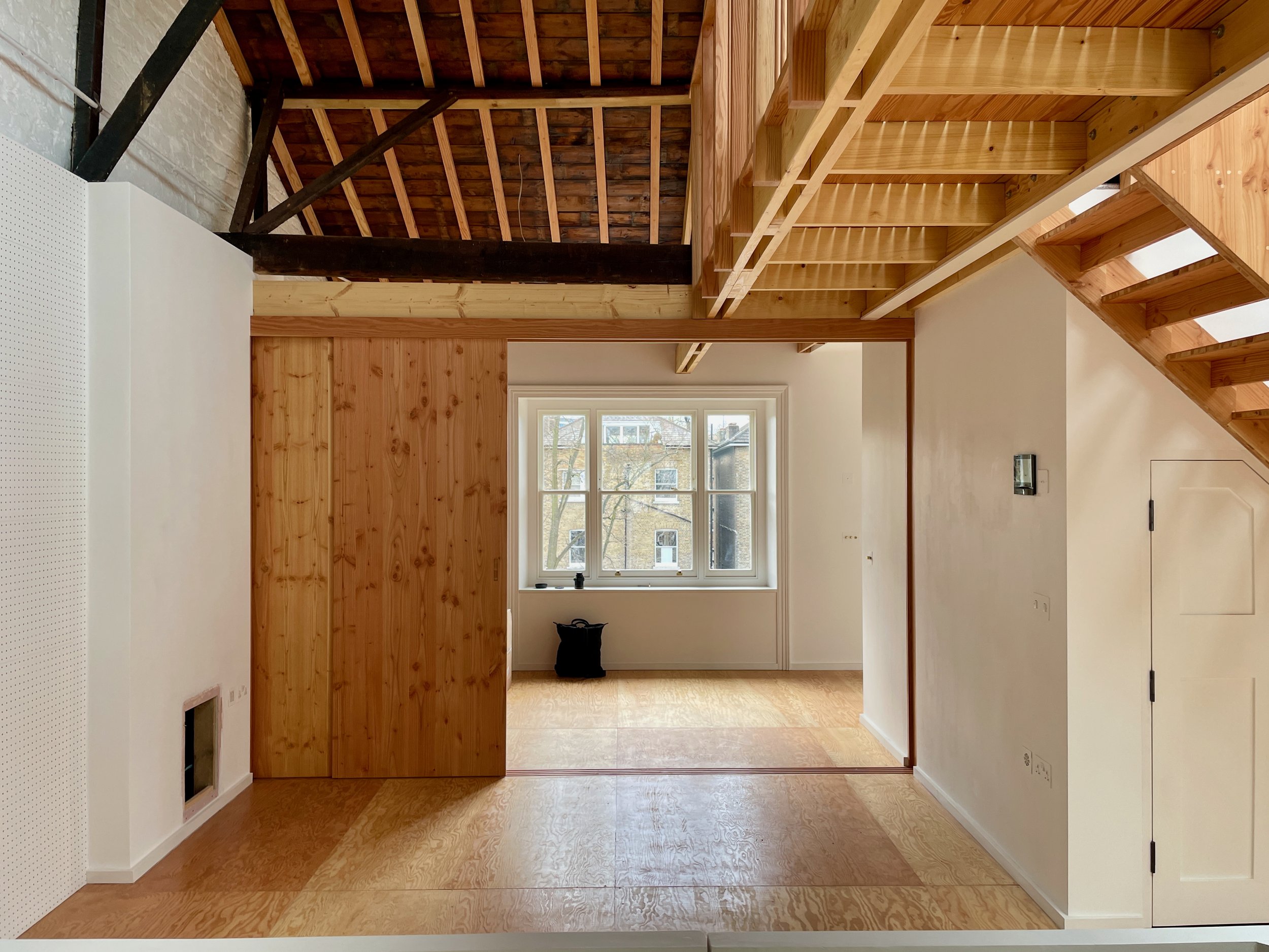 Open-plan interior with exposed timber beams, wood floors, and large central staircase leading to mezzanine level.