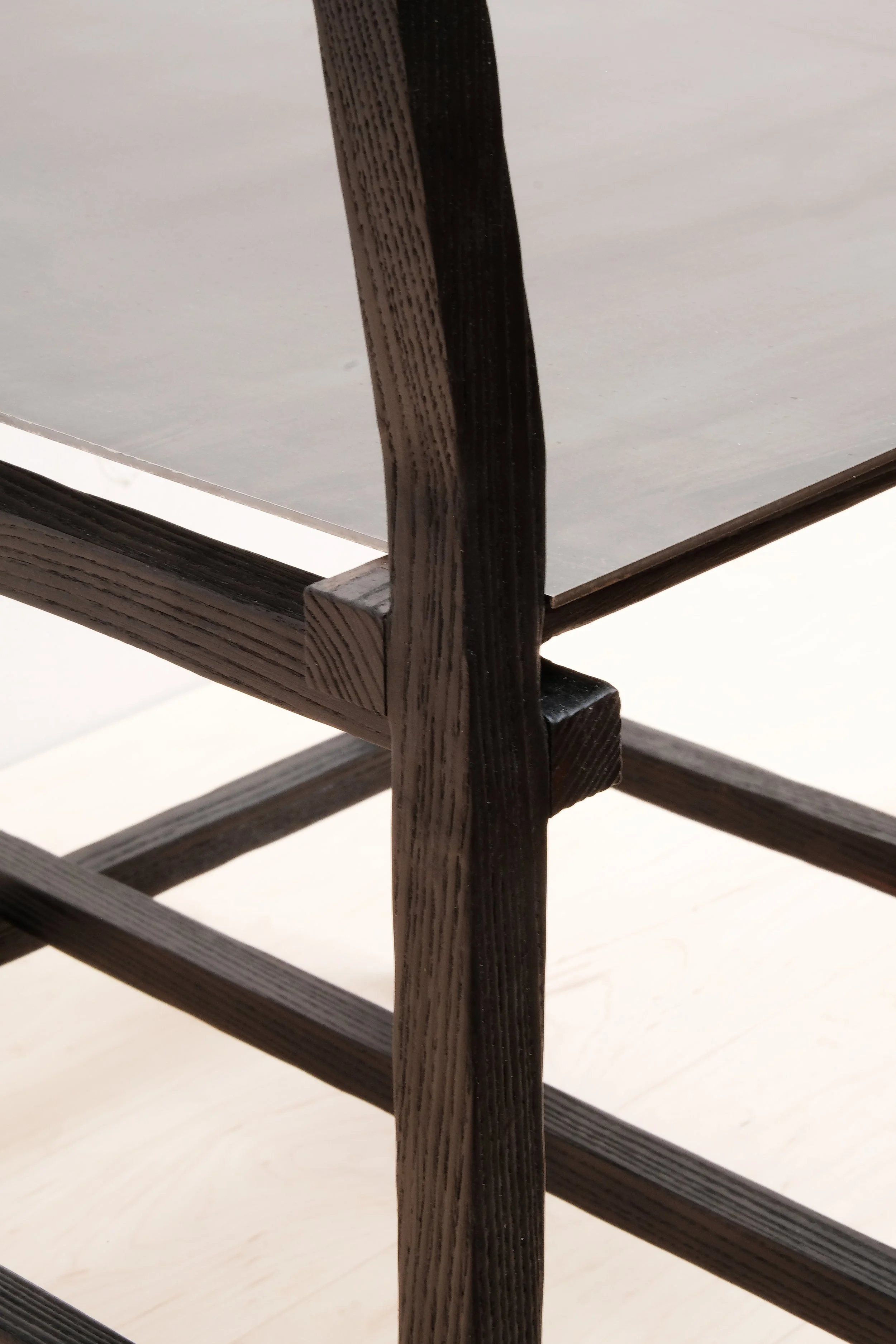 Close-up of the chair leg and seat connection, highlighting the textured black wood grain and precise craftsmanship.