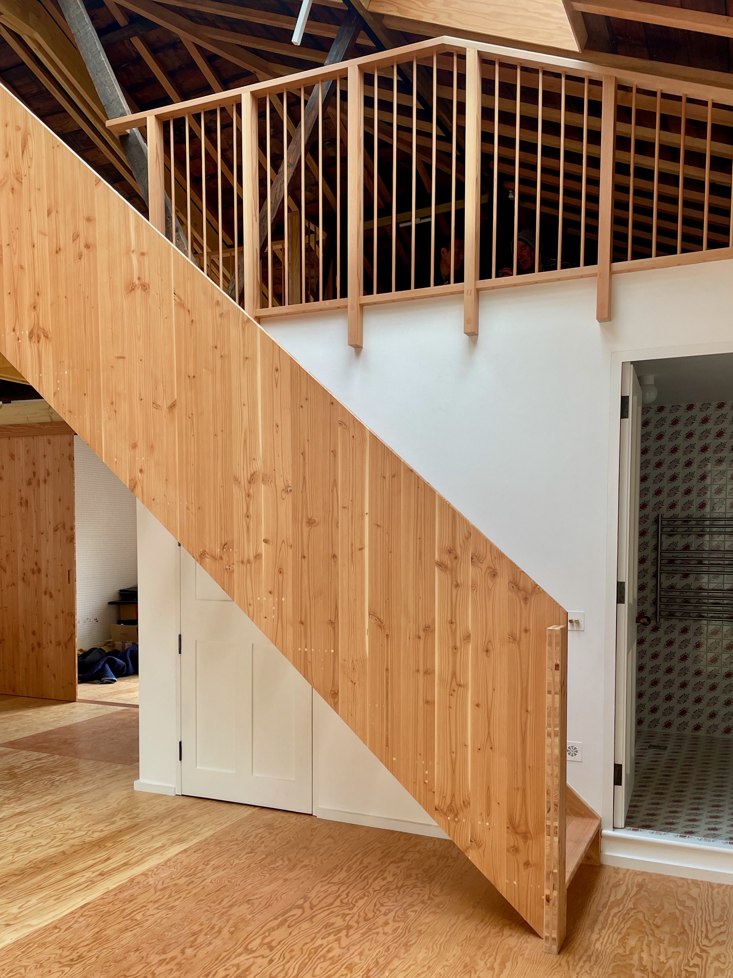 Angled view of a staircase with vertical timber balusters and a glimpse into a patterned-tile bathroom through an adjacent doorway.