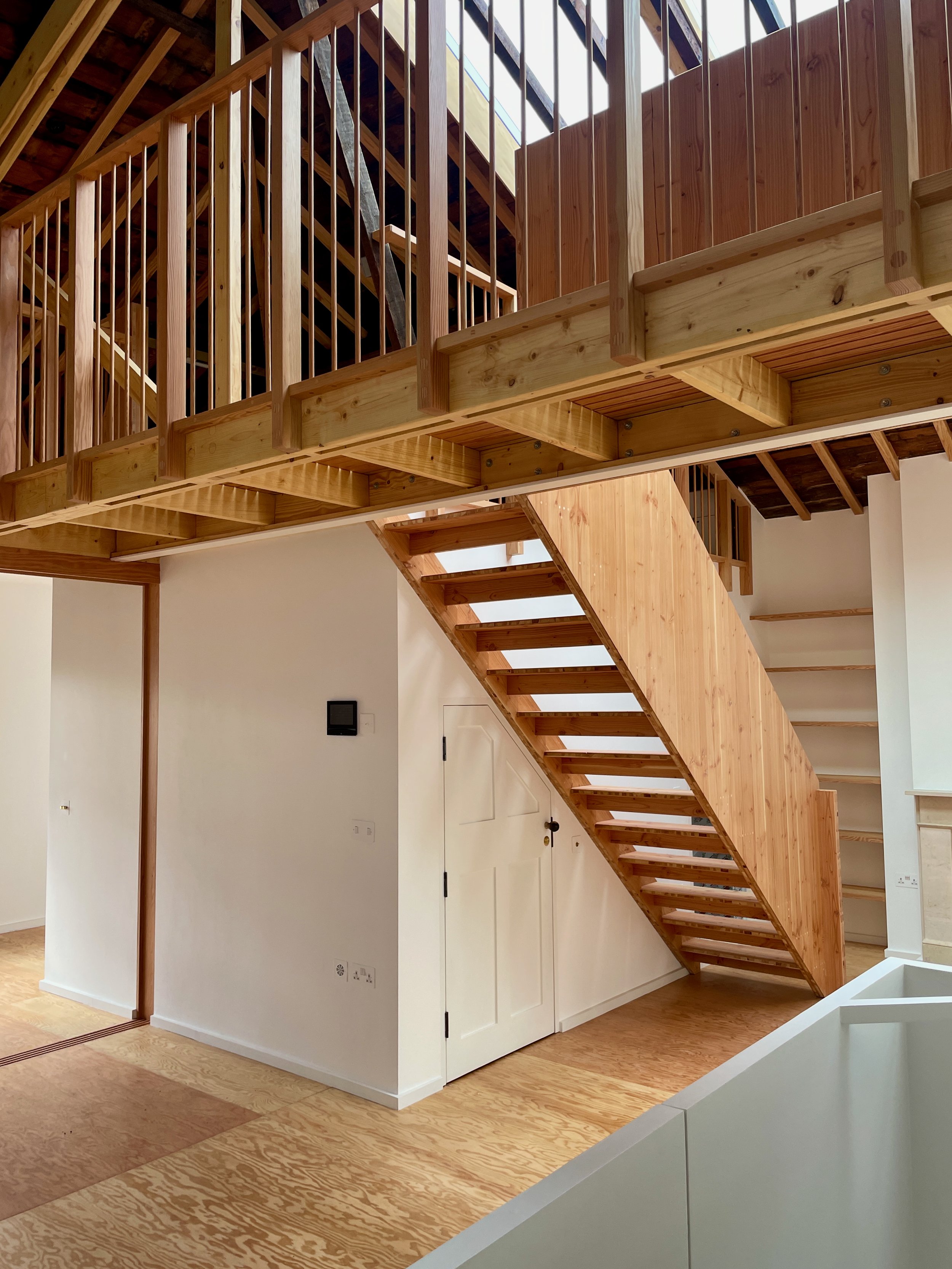 Timber staircase with under-stair door, leading to open mezzanine with wood railings and exposed ceiling beams.