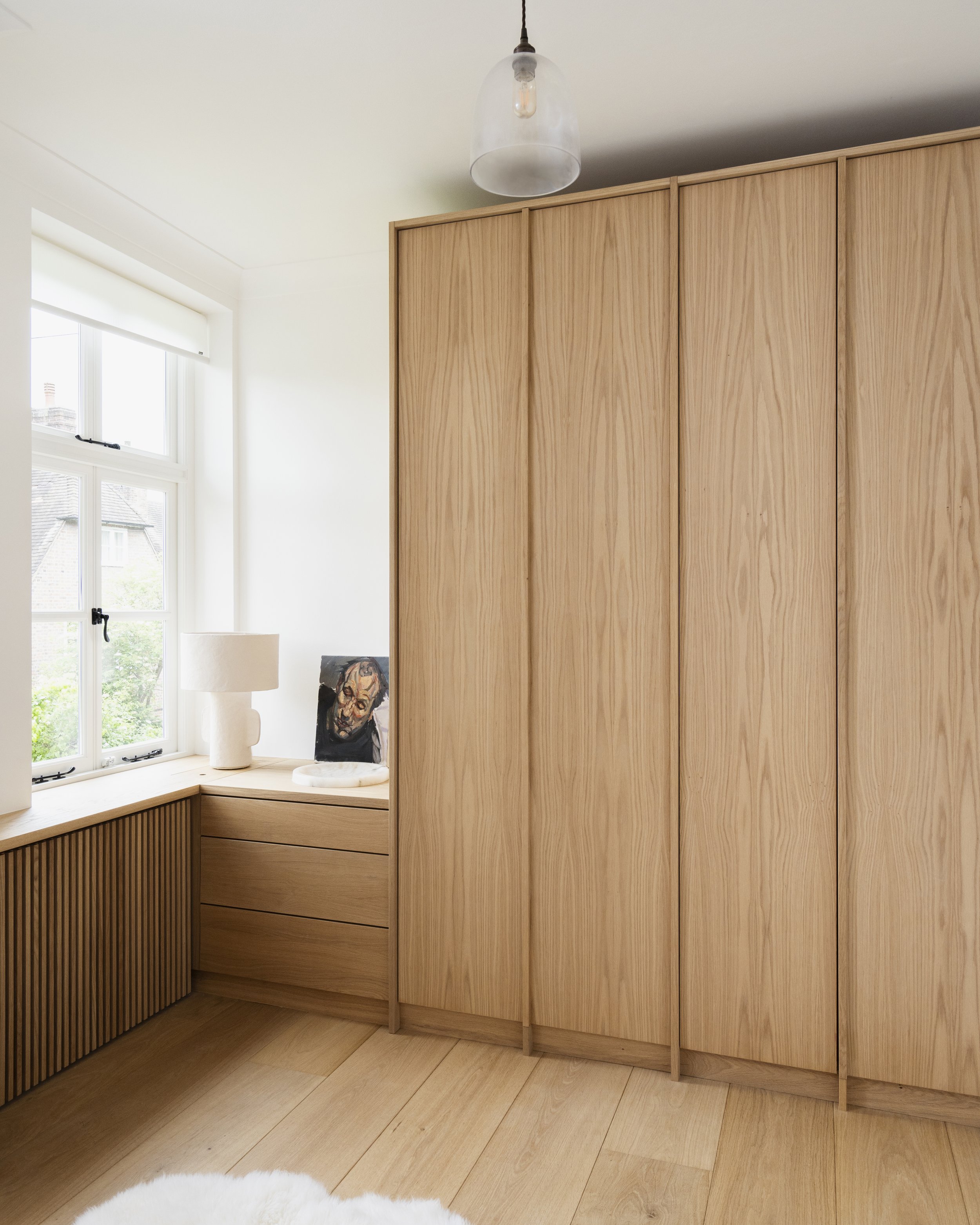 Light wood wardrobes and nook with vertical slatted radiator cover and soft natural light.