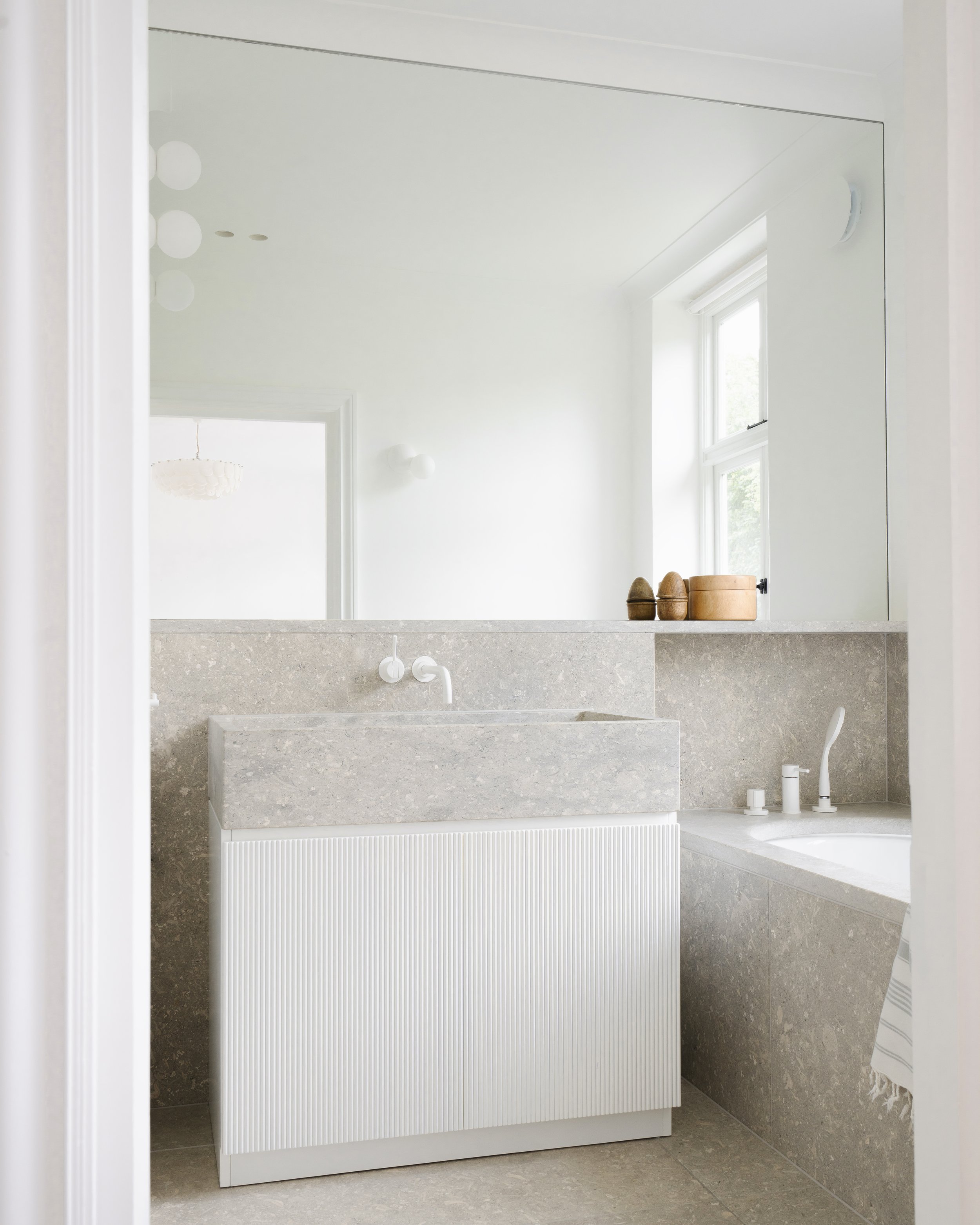 Minimalist bathroom vanity in fluted white detail with integrated limestone basin and wall-mounted tap.