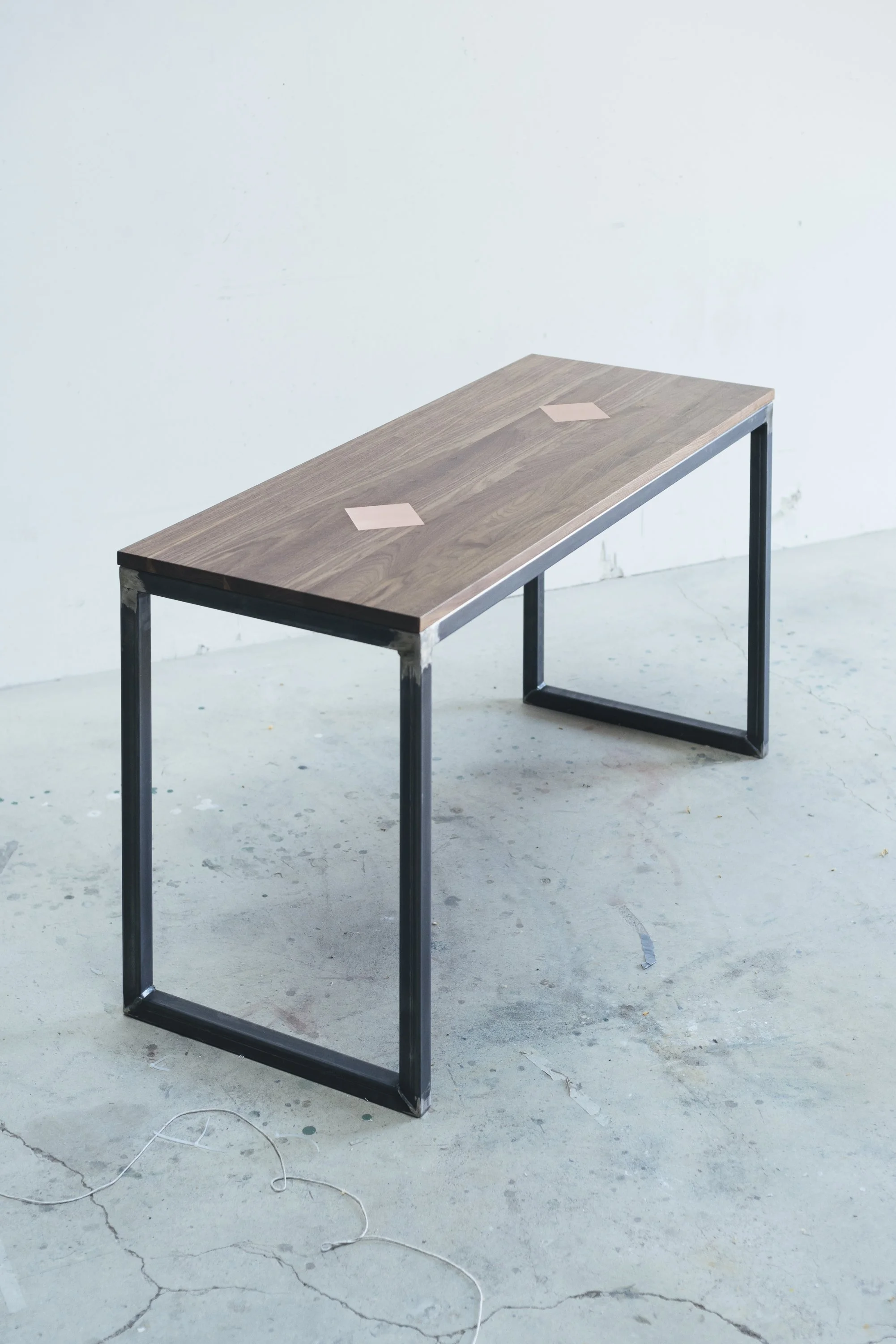 Angled view of the bench showing full length, metal frame, and wooden top with two copper square inlays.